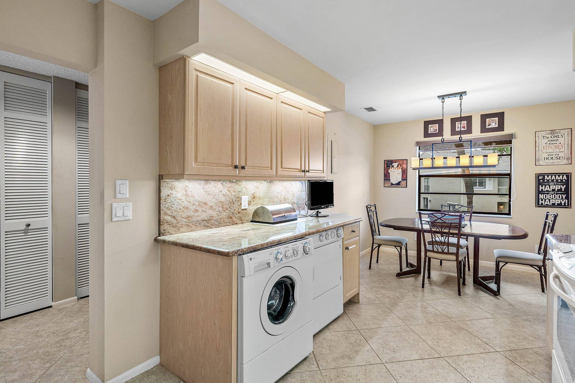 53 EASTGATE Drive, #B, Boynton Beach, FL 33436 Utility area featuring light-finish cabinetry, stone-surface countertops, stone-tile backsplash, and integrated laundry appliances, complemented by stone-finish tile flooring
