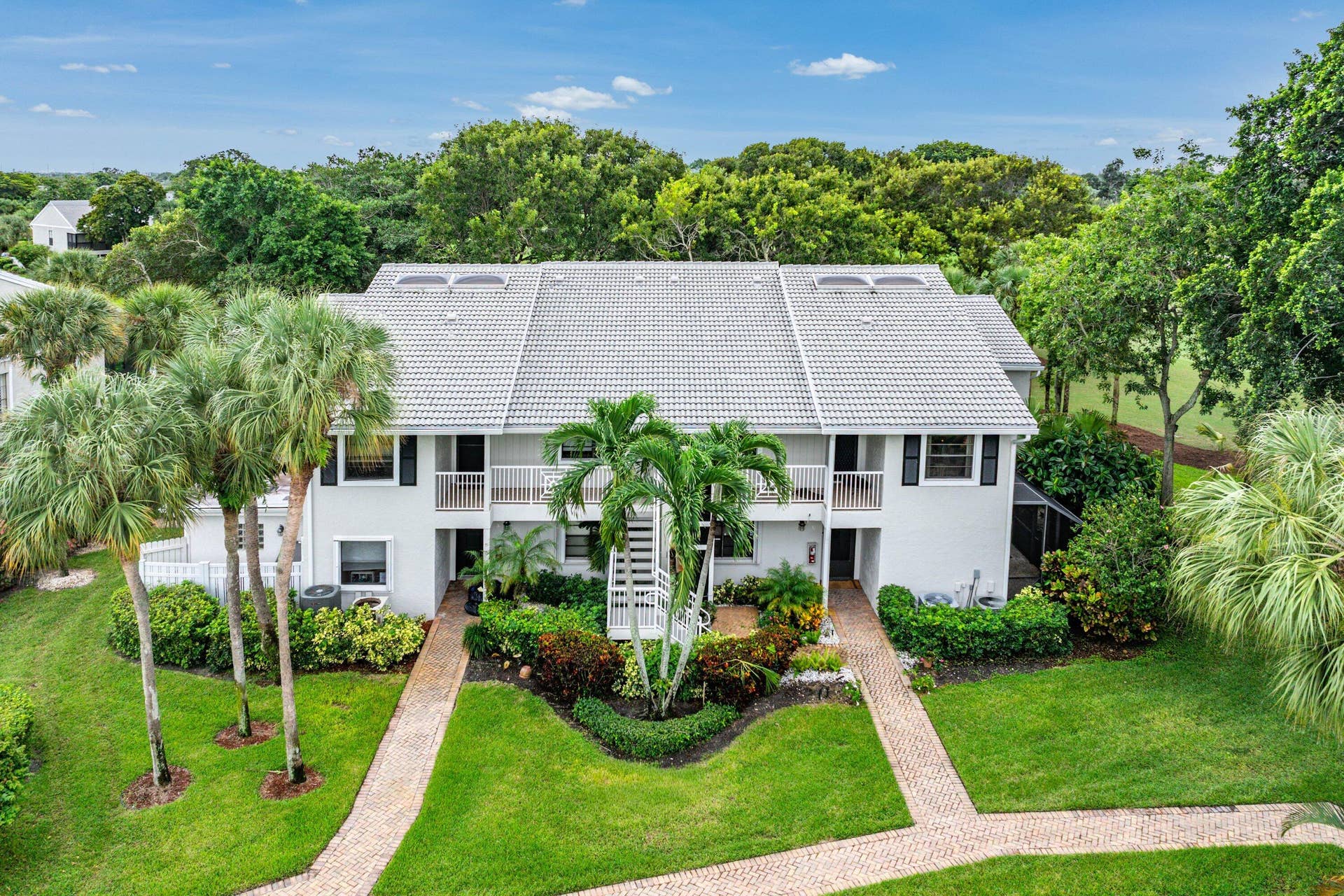 53 EASTGATE Drive, #B, Boynton Beach, FL 33436 Multi-story residence featuring a tile roof, brick paver walkways, mature palm trees, manicured landscaping, and second-level balcony railings