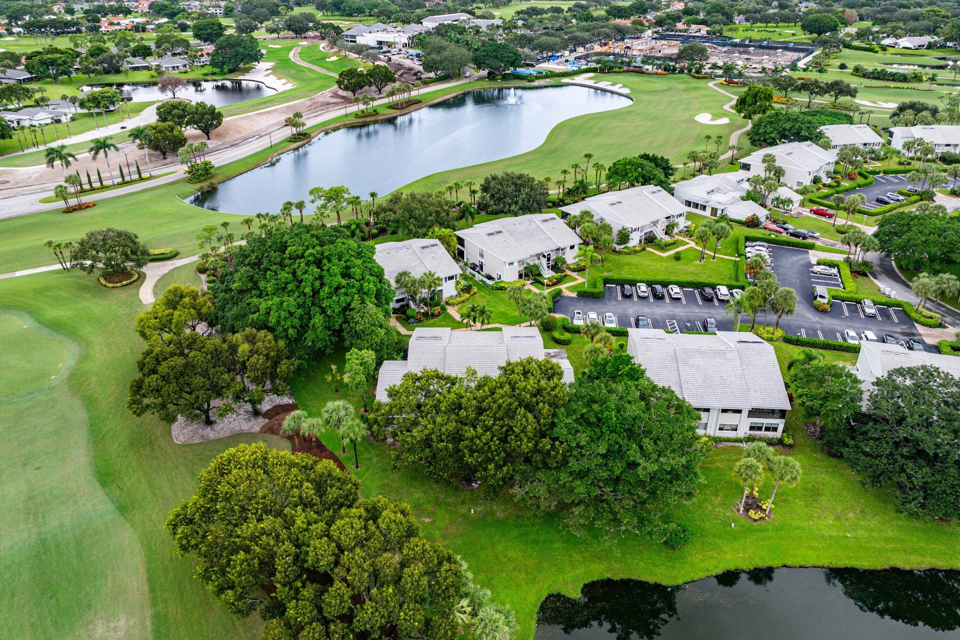 53 EASTGATE Drive, #B, Boynton Beach, FL 33436 Aerial perspective featuring multi-story residential buildings with tile roofing, expansive landscaped grounds, mature tree canopy, and proximity to a water feature and golf course