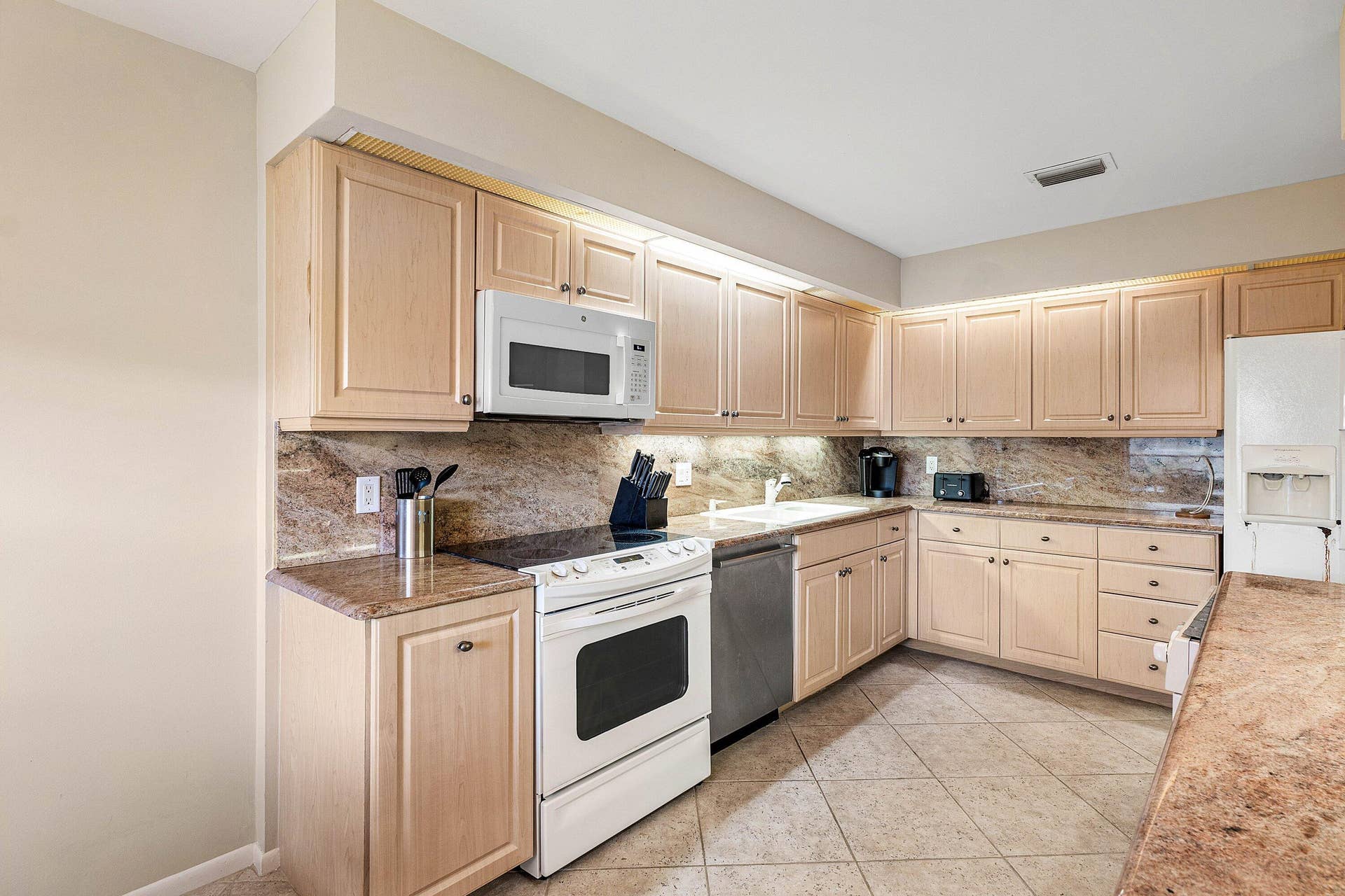 53 EASTGATE Drive, #B, Boynton Beach, FL 33436 Kitchen featuring light wood cabinetry, stone countertops, integrated under-cabinet lighting, tile flooring, and stainless steel dishwasher