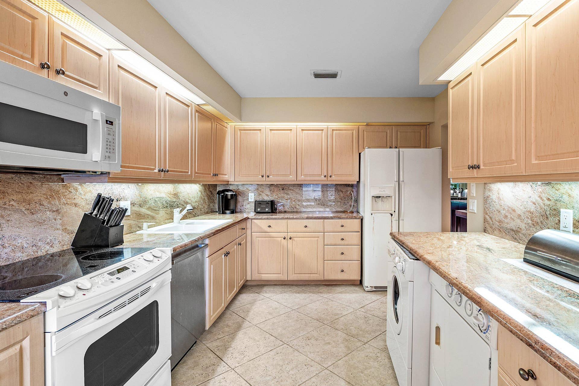 53 EASTGATE Drive, #B, Boynton Beach, FL 33436 Kitchen featuring shaker-style light wood cabinetry, stone countertops, integrated stone backsplash, ceramic tile flooring, and under-cabinet lighting