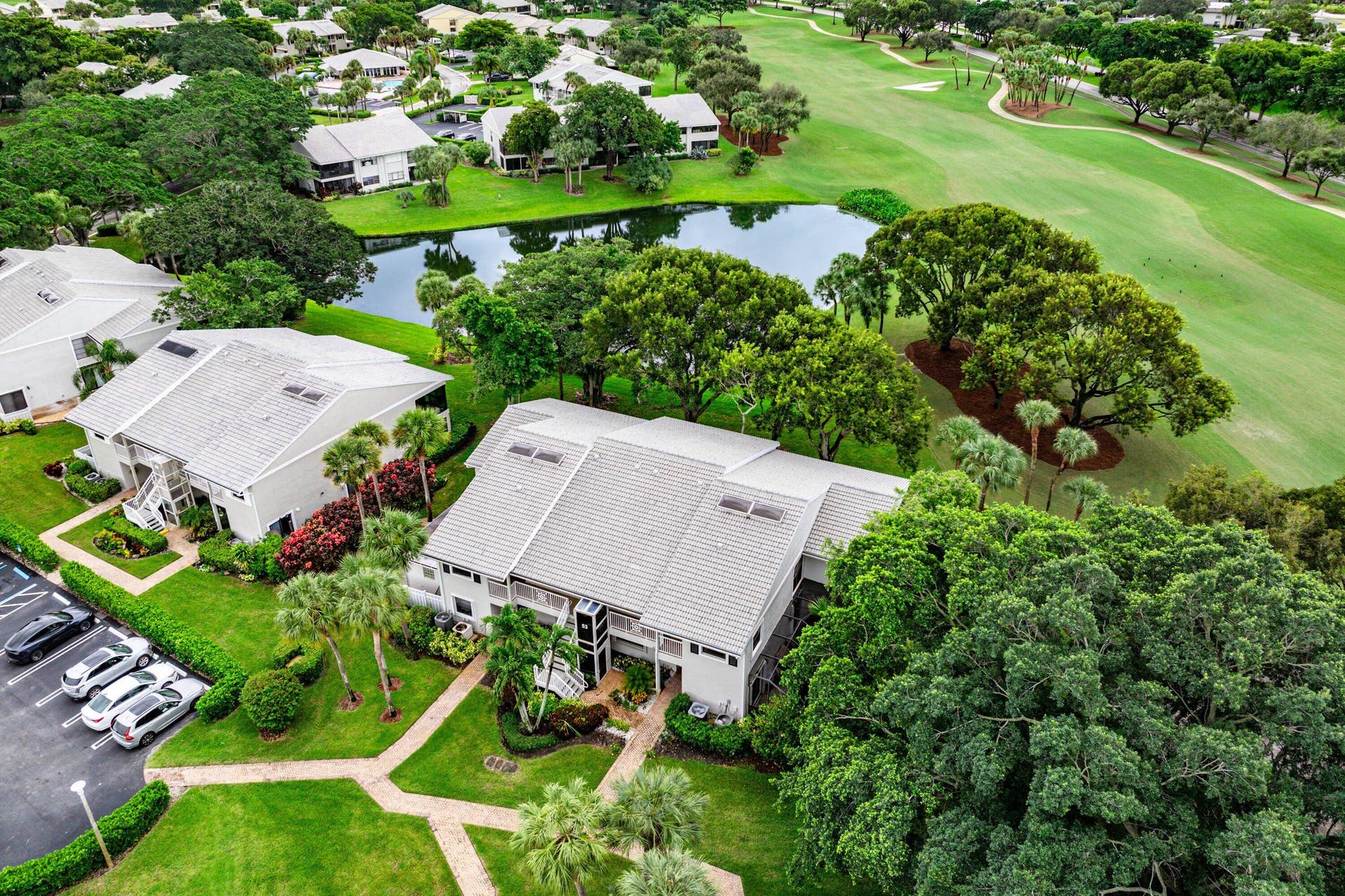 53 EASTGATE Drive, #B, Boynton Beach, FL 33436 Aerial perspective of multi-unit residential buildings featuring light-toned roof shingles, skylights, paver walkways, and mature landscaping situated along a pond and golf course fairways