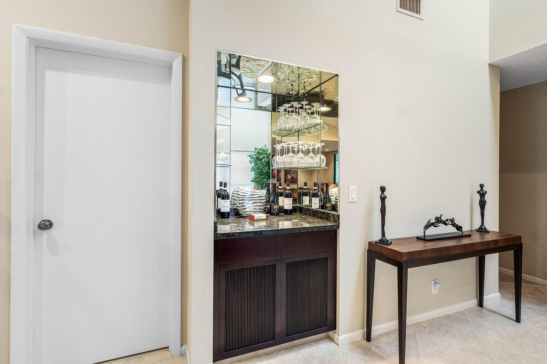 53 EASTGATE Drive, #B, Boynton Beach, FL 33436 Built-in wet bar featuring a stone countertop, dark wood cabinetry with slatted panel doors, integrated mirrored backsplash, and overhead glass shelving
