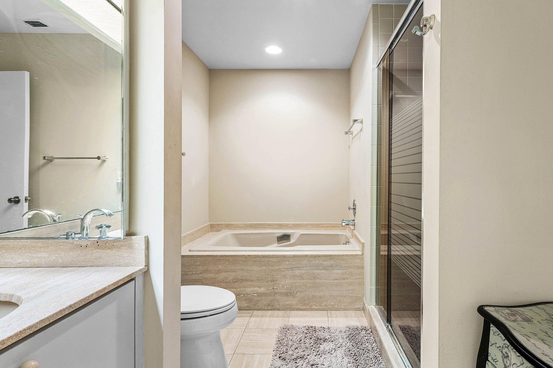 53 EASTGATE Drive, #B, Boynton Beach, FL 33436 Bathroom featuring a tiled soaking tub with a stone-surround deck, separate glass-enclosed shower, vanity with stone countertop, and wall-to-wall mirror