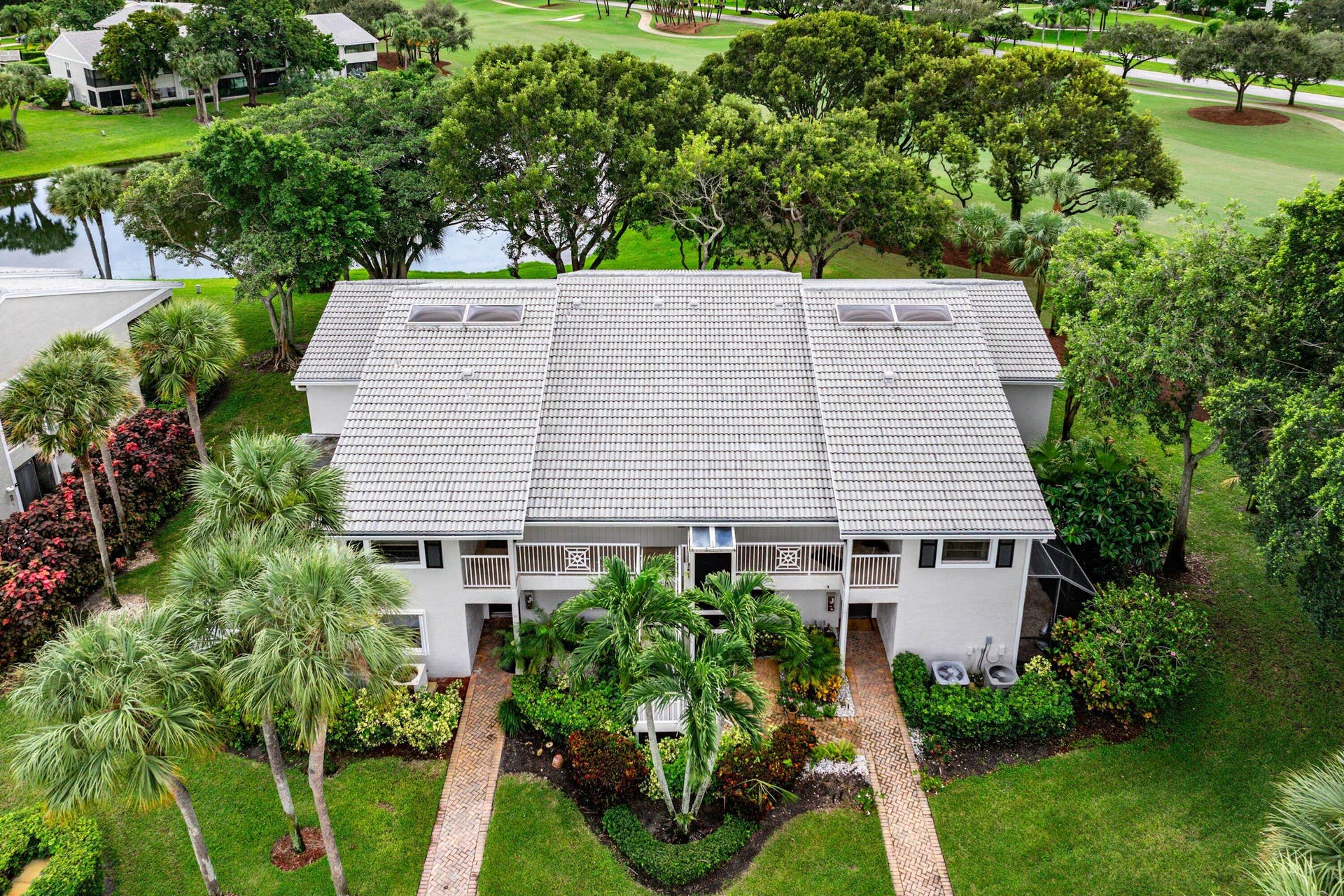 53 EASTGATE Drive, #B, Boynton Beach, FL 33436 Two-story multi-unit structure featuring a tile roof, dual balconies, brick-paver walkways, and exterior landscaping, positioned on a golf course with water features