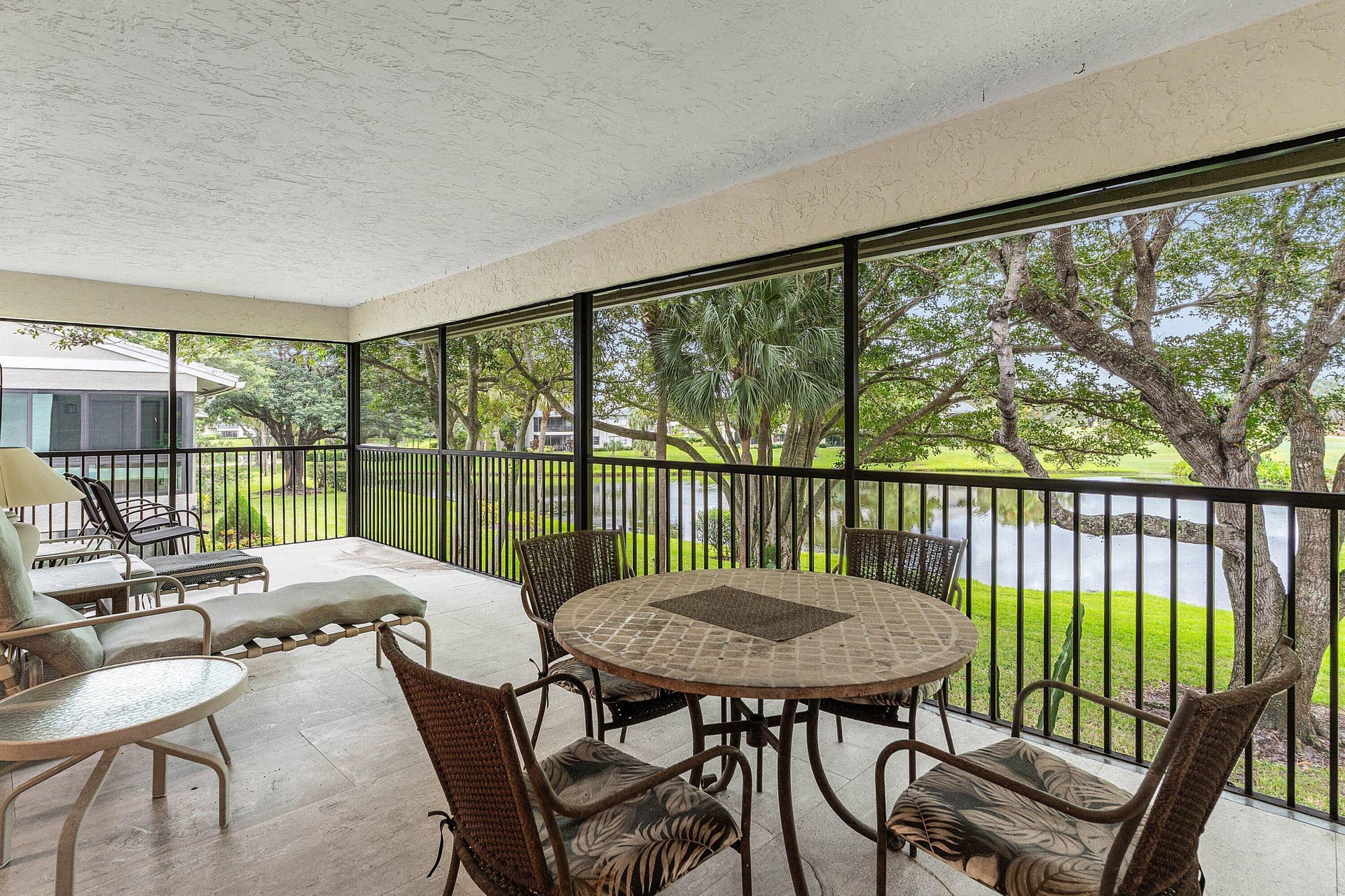 53 EASTGATE Drive, #B, Boynton Beach, FL 33436 Screened-in lanai featuring tile flooring, a textured ceiling, and metal railings overlooking a water feature and mature trees