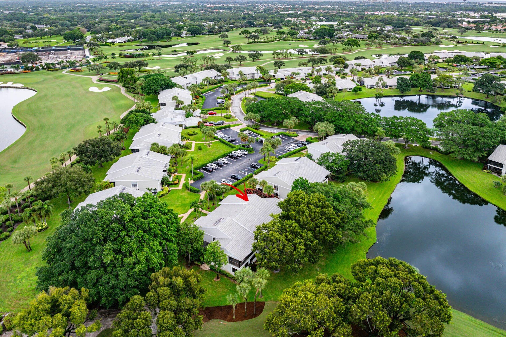53 EASTGATE Drive, #B, Boynton Beach, FL 33436 Aerial perspective of a multi-unit property featuring a shingle roof, paved surface parking, mature landscaping, and proximity to water elements and golf course grounds