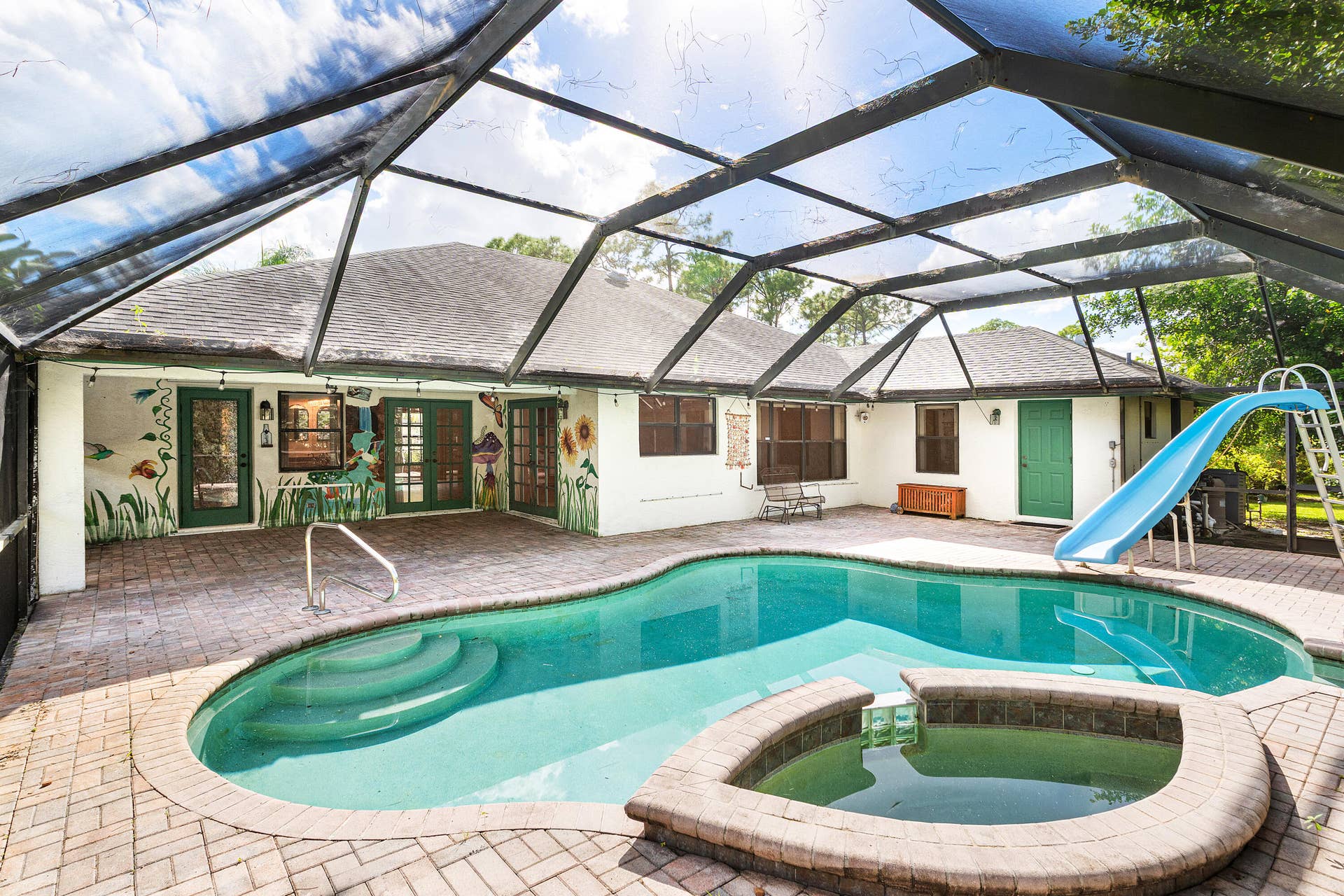 13677 Citrus Grove Boulevard, West Palm Beach, FL 33412 Screened-in patio featuring a brick-paver deck, an in-ground pool with integrated spillover spa, and a built-in water slide