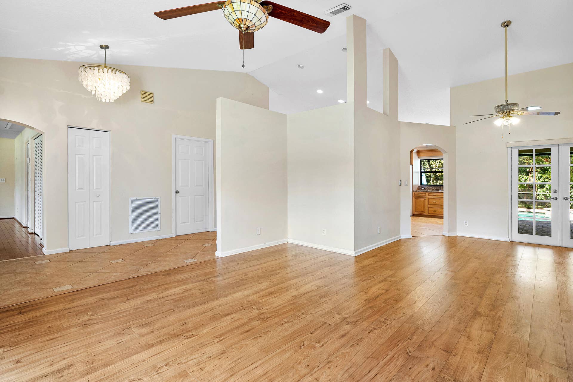 13677 Citrus Grove Boulevard, West Palm Beach, FL 33412 Open-concept room featuring vaulted ceilings, wood-finish flooring, dual ceiling fans, a crystal-style chandelier, and glass-paneled double doors