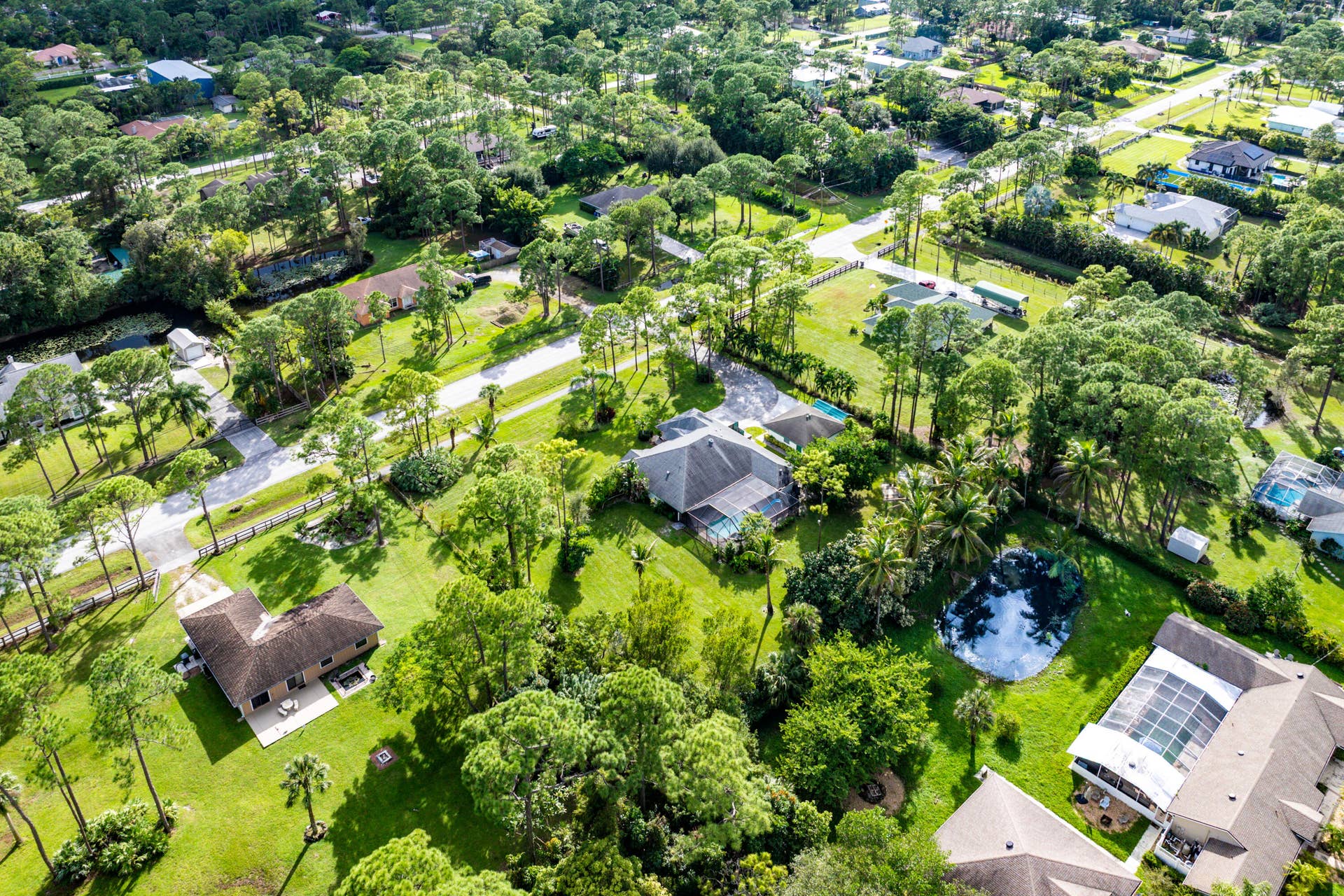 13677 Citrus Grove Boulevard, West Palm Beach, FL 33412 Aerial perspective featuring expansive residential lots, mature tree canopy, integrated ponds, and multi-pitched rooflines