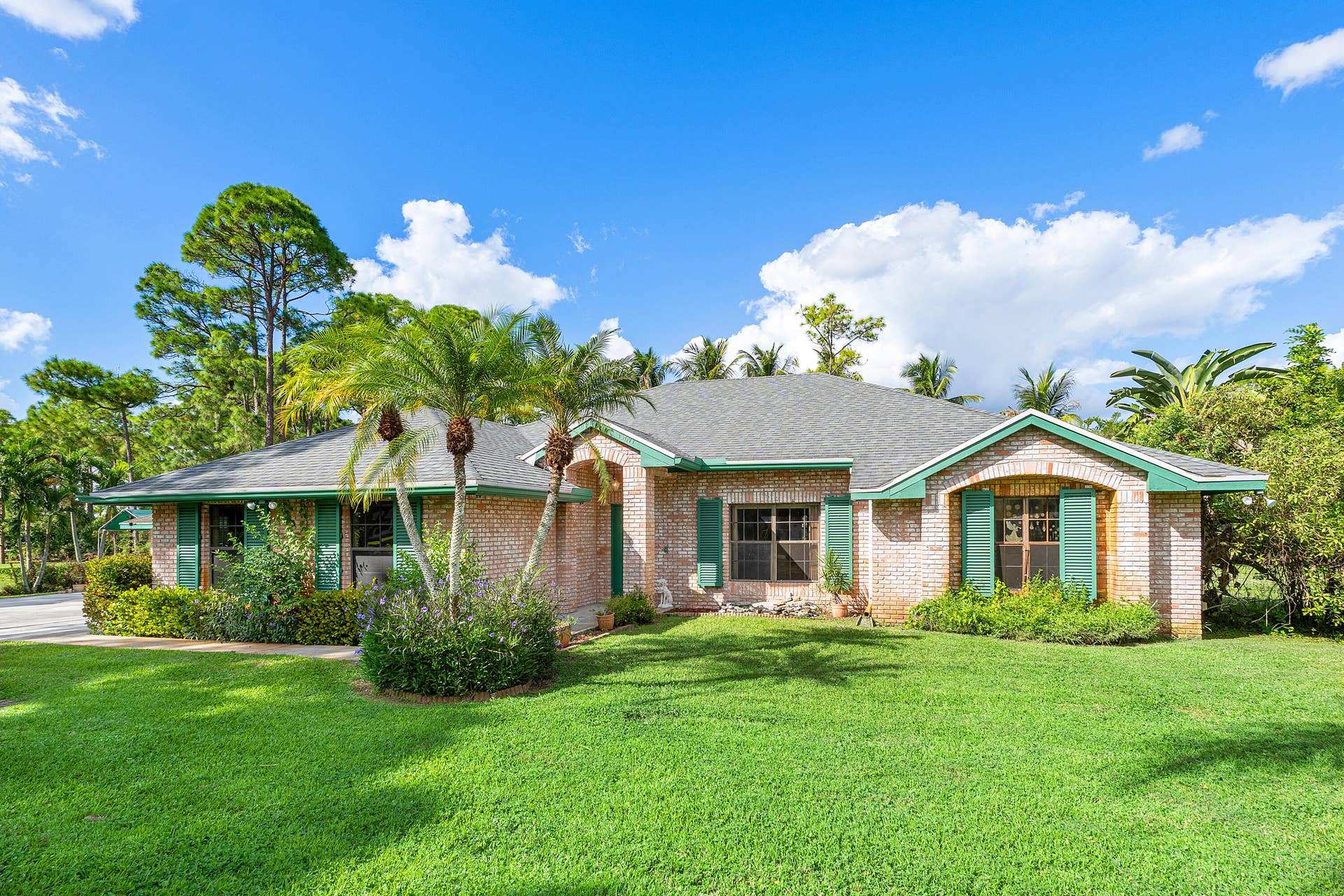 13677 Citrus Grove Boulevard, West Palm Beach, FL 33412 Single-story brick exterior featuring a multi-gabled roofline, green shutters, arched window accents, and manicured landscaping