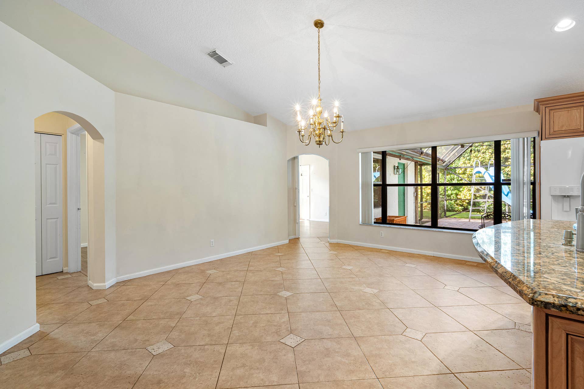 13677 Citrus Grove Boulevard, West Palm Beach, FL 33412 Open interior featuring vaulted ceilings, tile flooring with decorative inserts, a central multi-arm chandelier, arched entryways, and a large multi-pane window