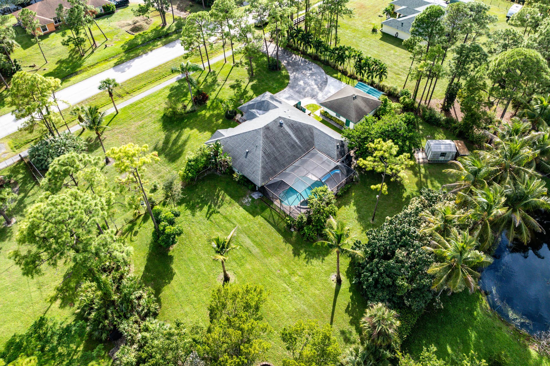 13677 Citrus Grove Boulevard, West Palm Beach, FL 33412 Aerial perspective of a sprawling corner lot featuring a screened-in pool, shingle roof architecture, a detached garage, and mature landscaping