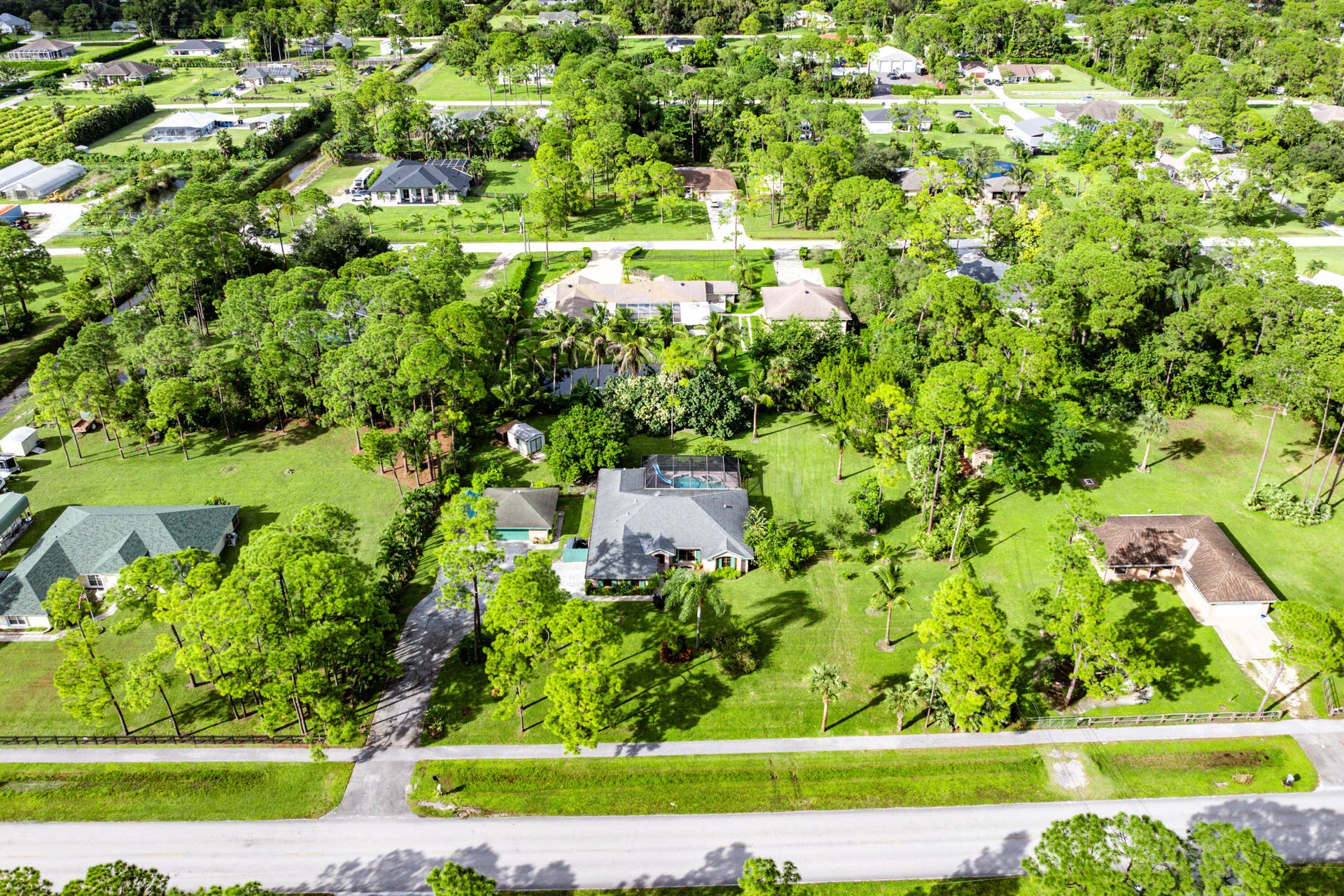 13677 Citrus Grove Boulevard, West Palm Beach, FL 33412 Aerial perspective of a sprawling property featuring a multi-gabled residence, an enclosed pool area, a detached auxiliary structure, and expansive grounds with mature trees