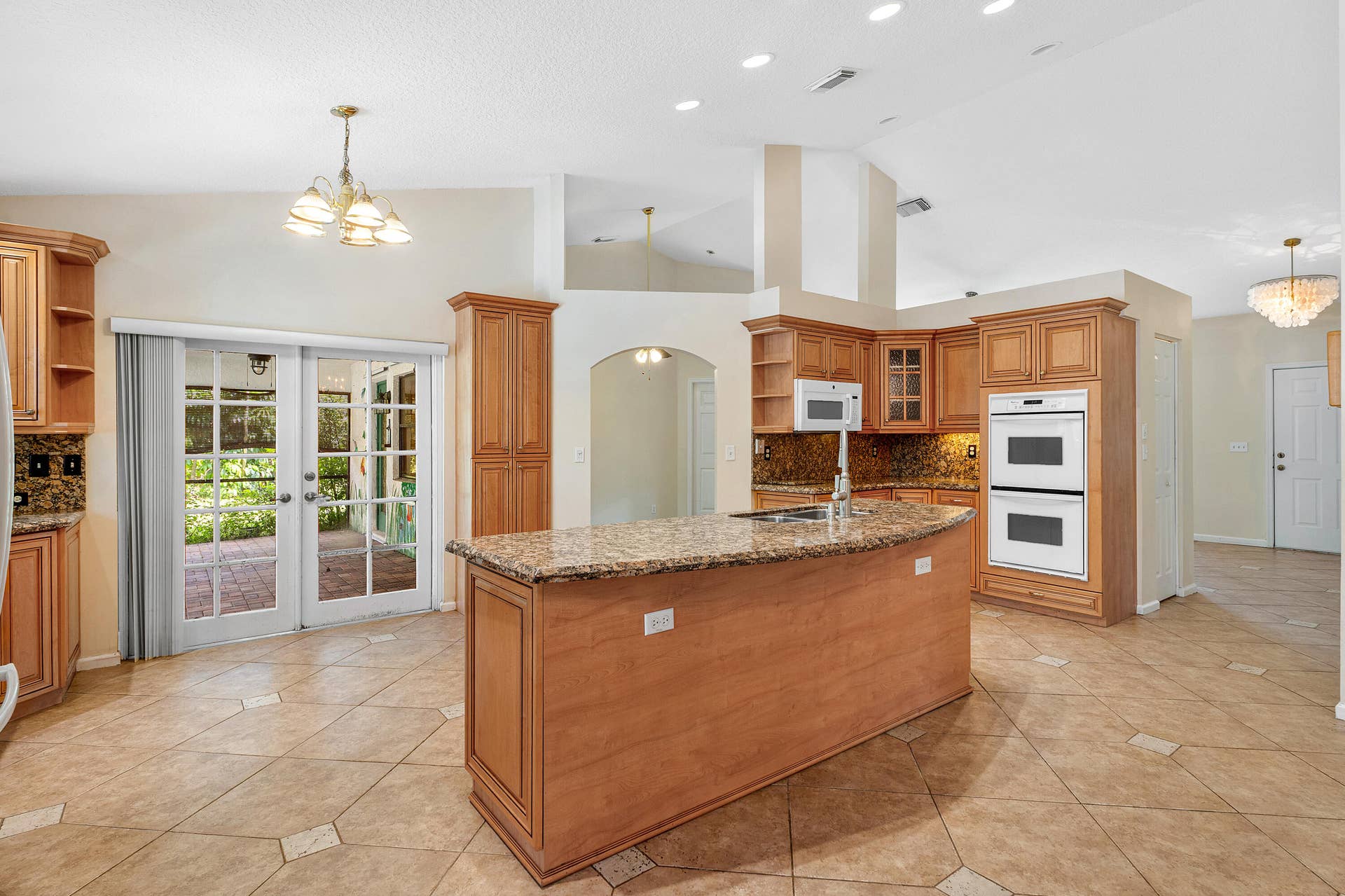13677 Citrus Grove Boulevard, West Palm Beach, FL 33412 Kitchen featuring wood cabinetry, a stone-surfaced center island, double wall ovens, vaulted ceilings, and tile flooring