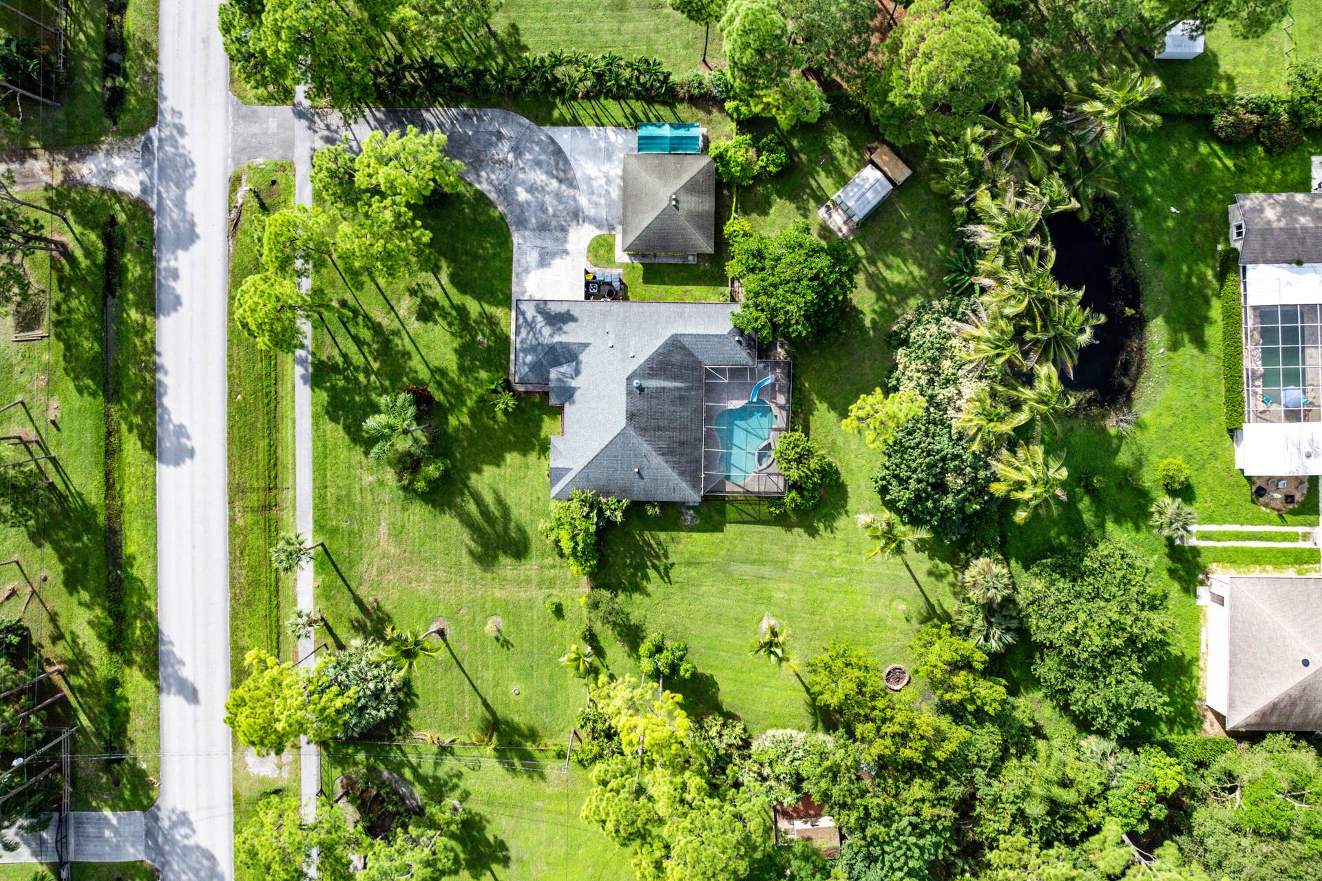 13677 Citrus Grove Boulevard, West Palm Beach, FL 33412 Aerial view of a sprawling lot featuring a multi-gabled roofline, a screened-in pool, a paved driveway, and mature landscaping
