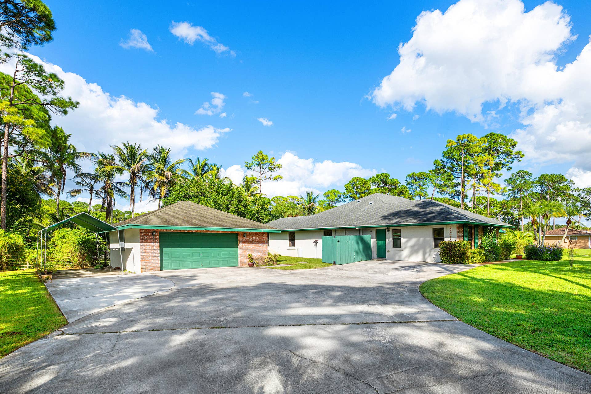 13677 Citrus Grove Boulevard, West Palm Beach, FL 33412 Exterior featuring a detached 2.5 car-garage with an attached carport, brick veneer detailing, a concrete driveway, and expansive lawn space