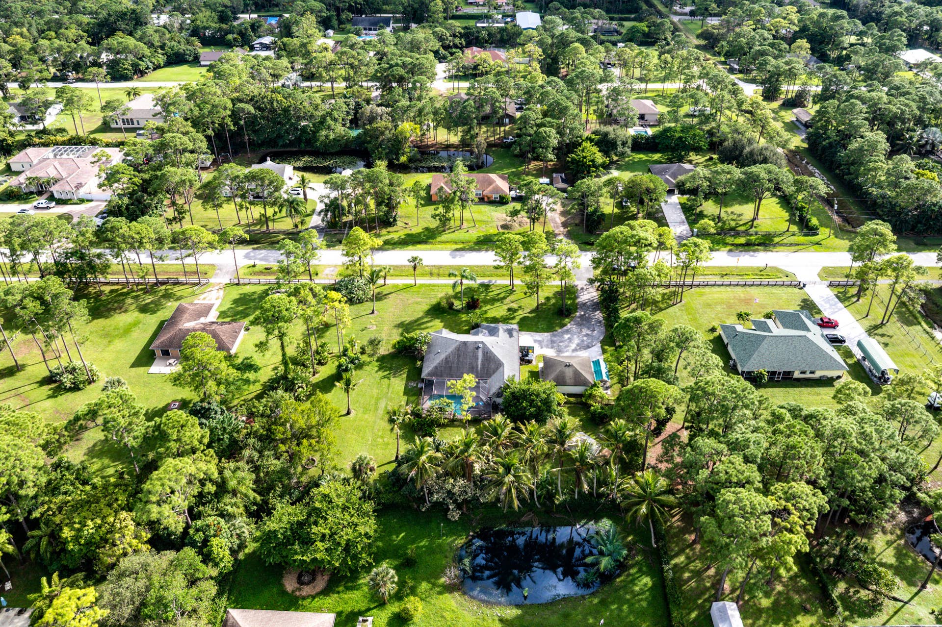 13677 Citrus Grove Boulevard, West Palm Beach, FL 33412 Aerial perspective of a multi-structure property featuring a detached swimming pool, paved driveway, mature trees, and a private pond