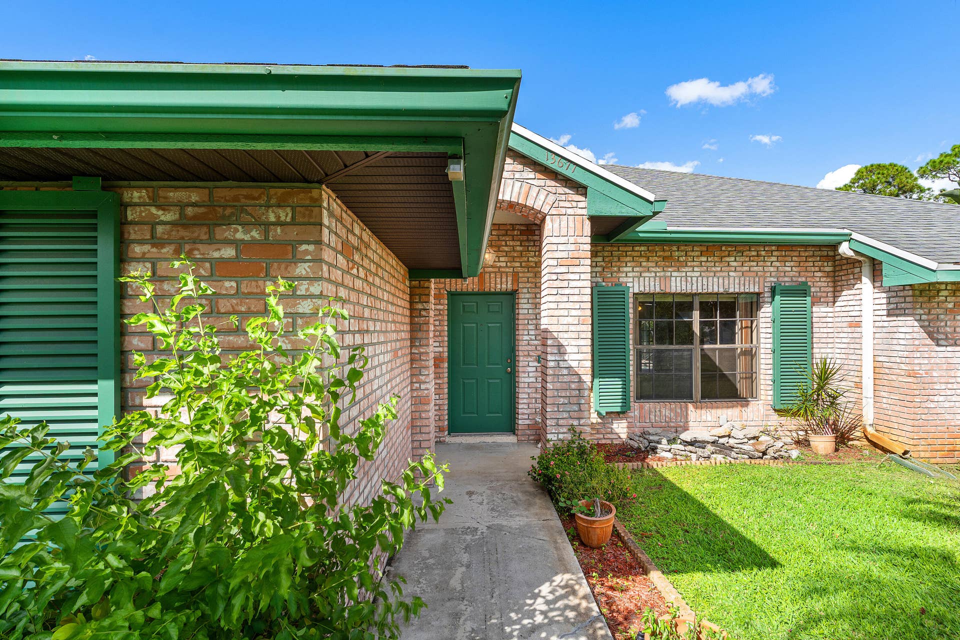 13677 Citrus Grove Boulevard, West Palm Beach, FL 33412 Brick exterior featuring a recessed entry, arched masonry detail, green louvered shutters, and a concrete walkway