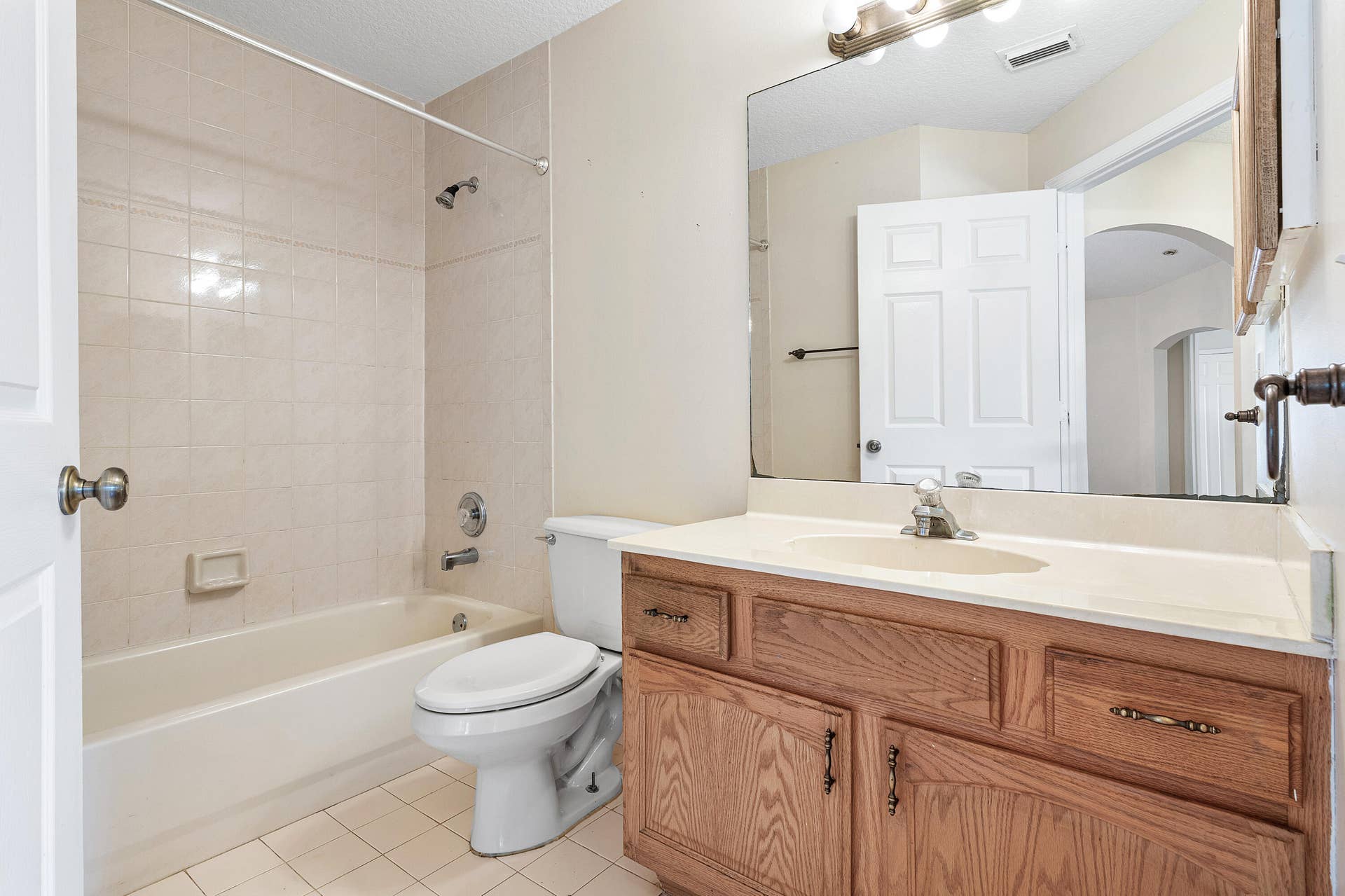 13677 Citrus Grove Boulevard, West Palm Beach, FL 33412 Guest bathroom featuring a wood-finish vanity with an integrated countertop, large wall-mounted mirror, ceramic tile flooring, and a shower-tub combination with tile surround