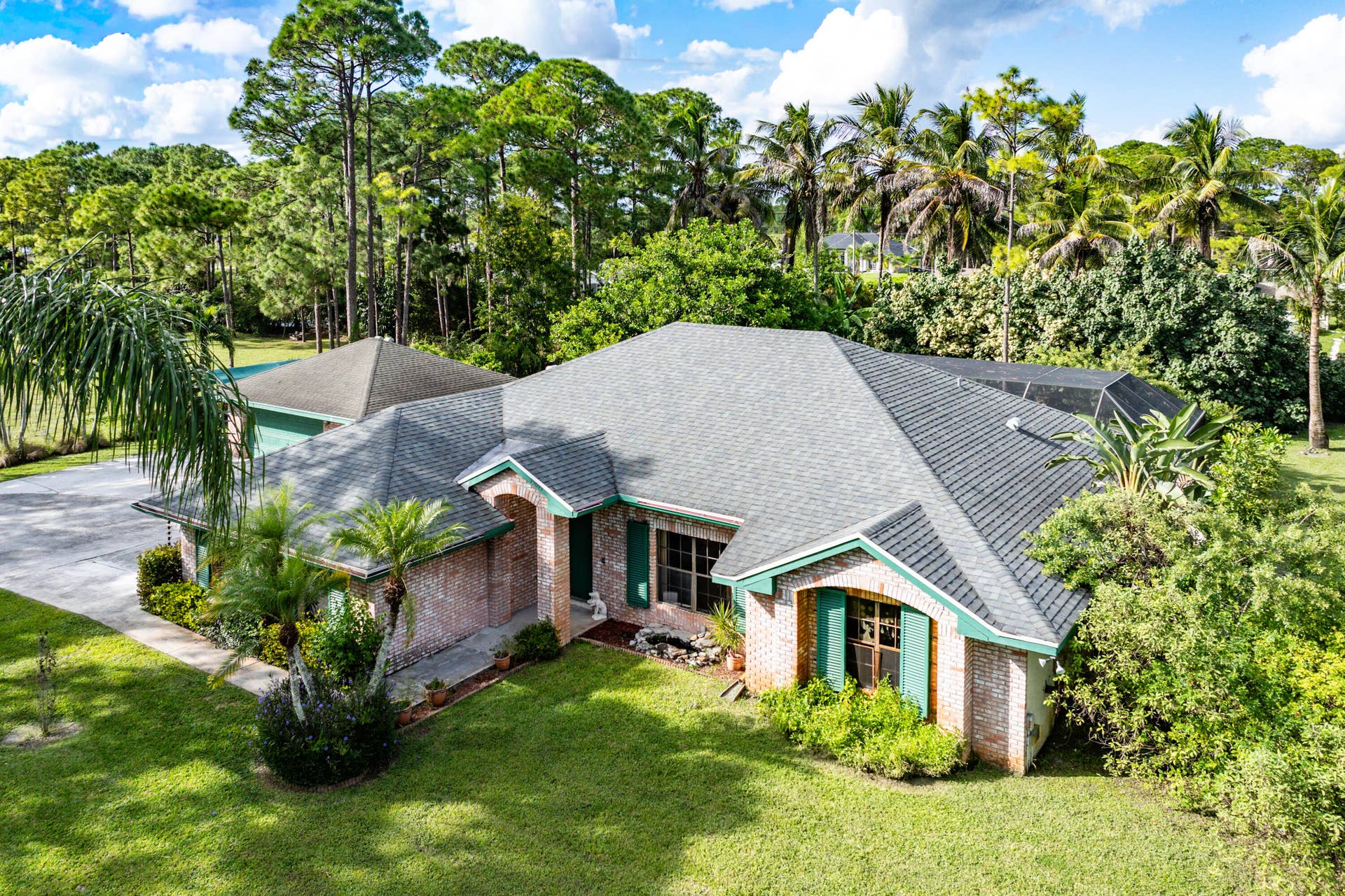 13677 Citrus Grove Boulevard, West Palm Beach, FL 33412 Single-story brick exterior featuring a multi-gabled asphalt shingle roof, attached garage, and decorative shutters on a lot with mature landscaping