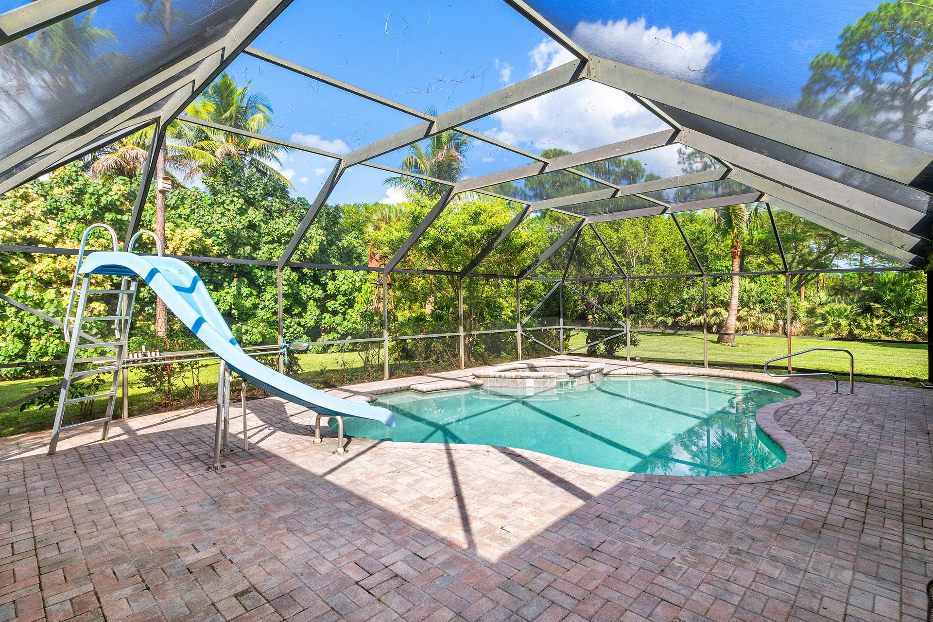13677 Citrus Grove Boulevard, West Palm Beach, FL 33412 Screened-in pool enclosure featuring paver decking, an integrated pool slide, and an in-ground spa