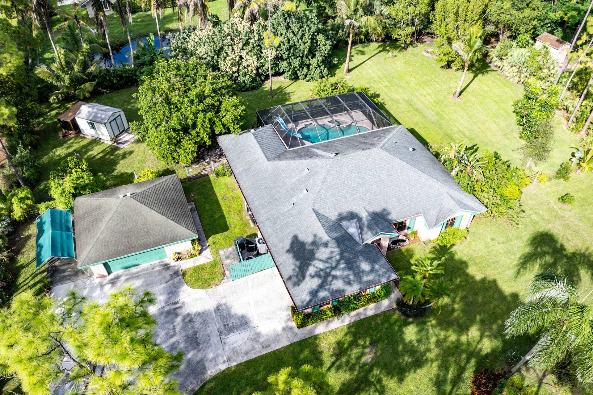 13677 Citrus Grove Boulevard, West Palm Beach, FL 33412 Aerial perspective of a property featuring an expansive lawn, a detached storage structure, a screen-enclosed pool, and a paved driveway
