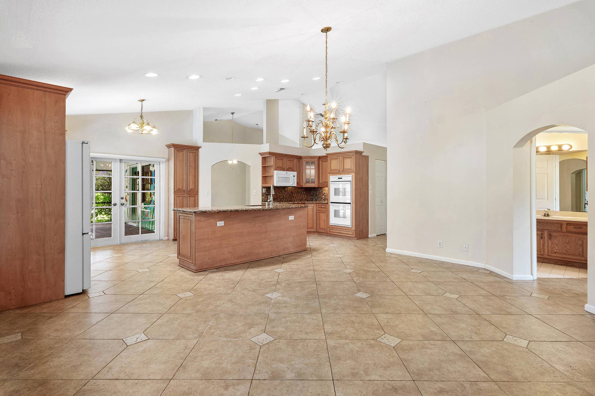 13677 Citrus Grove Boulevard, West Palm Beach, FL 33412 Open-concept interior featuring vaulted ceilings, tile flooring with decorative inserts, a kitchen island, recessed lighting, and ornate chandeliers