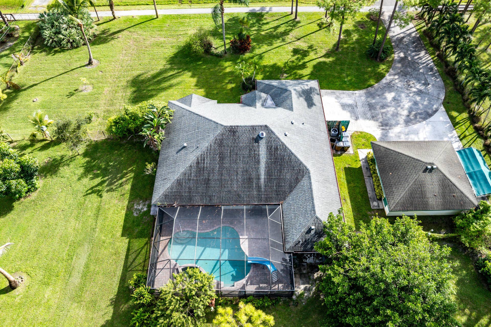 13677 Citrus Grove Boulevard, West Palm Beach, FL 33412 Aerial view of a property featuring an expansive manicured lawn, a detached garage, a paved circular driveway, and a screened-in swimming pool with an integrated slide
