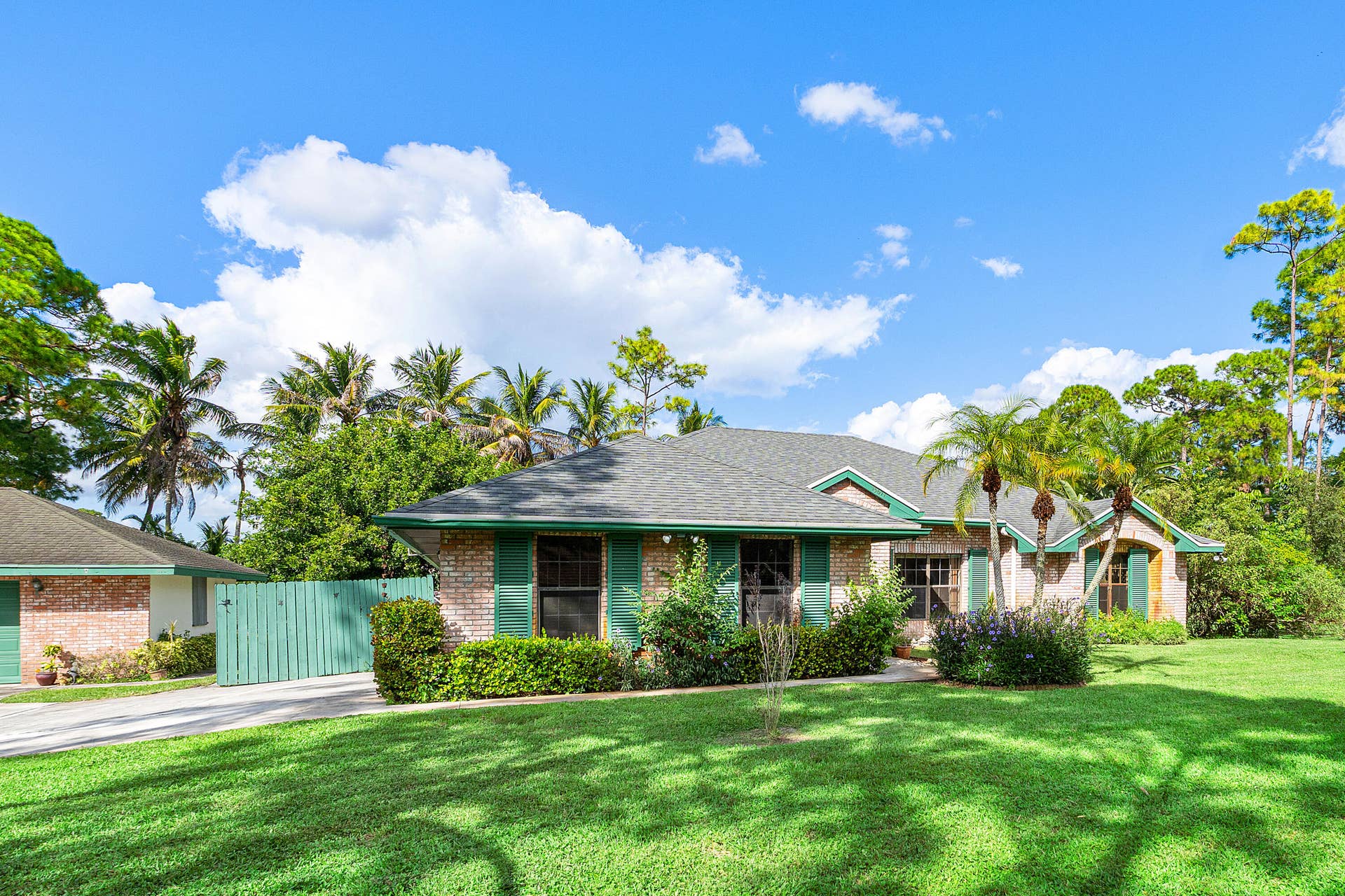 13677 Citrus Grove Boulevard, West Palm Beach, FL 33412 Single-story residence featuring a brick facade, architectural shingle roof, green shutter accents, and a concrete driveway
