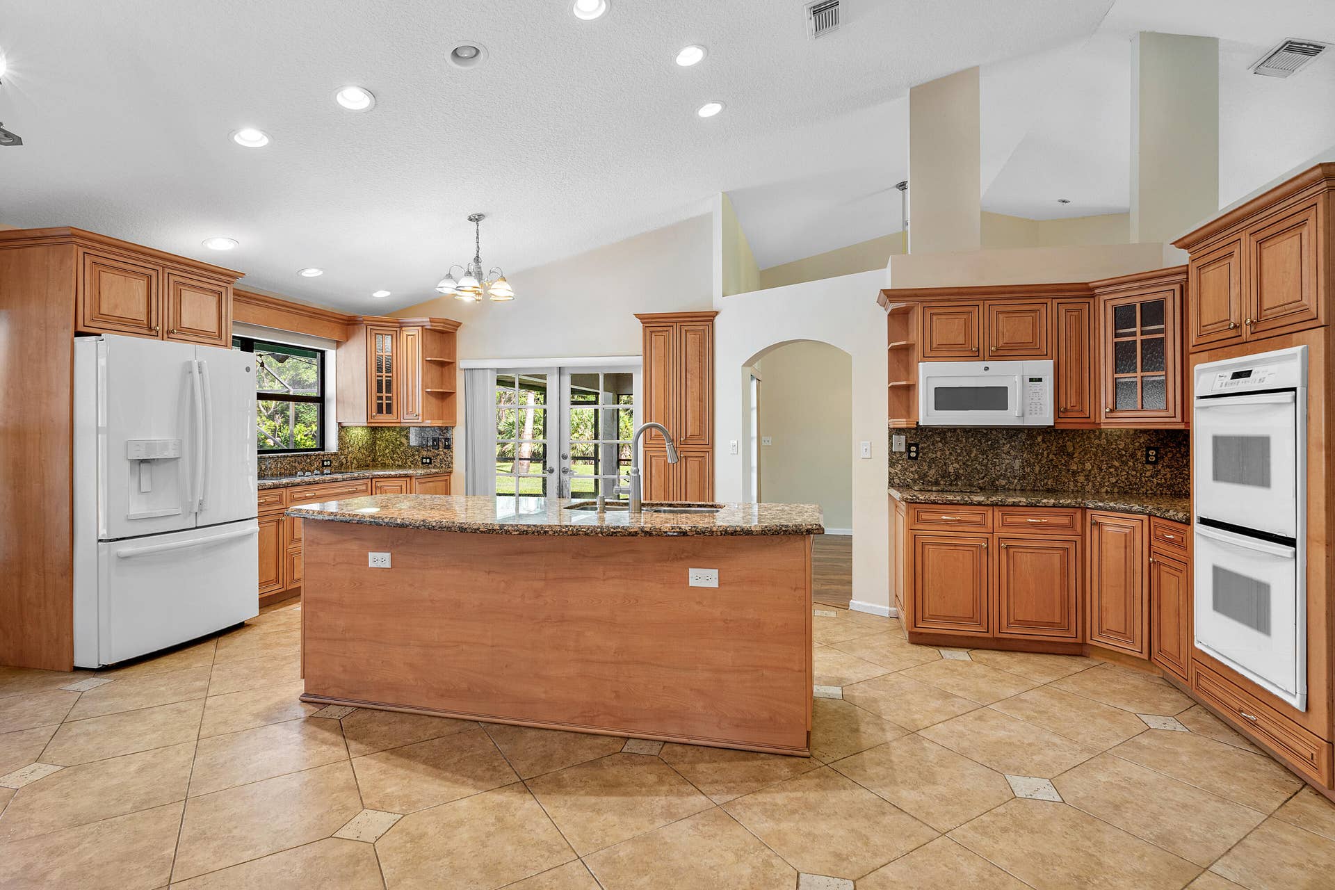 13677 Citrus Grove Boulevard, West Palm Beach, FL 33412 Kitchen featuring custom wood cabinetry, stone countertops, central island with sink, built-in double wall oven, and tile flooring