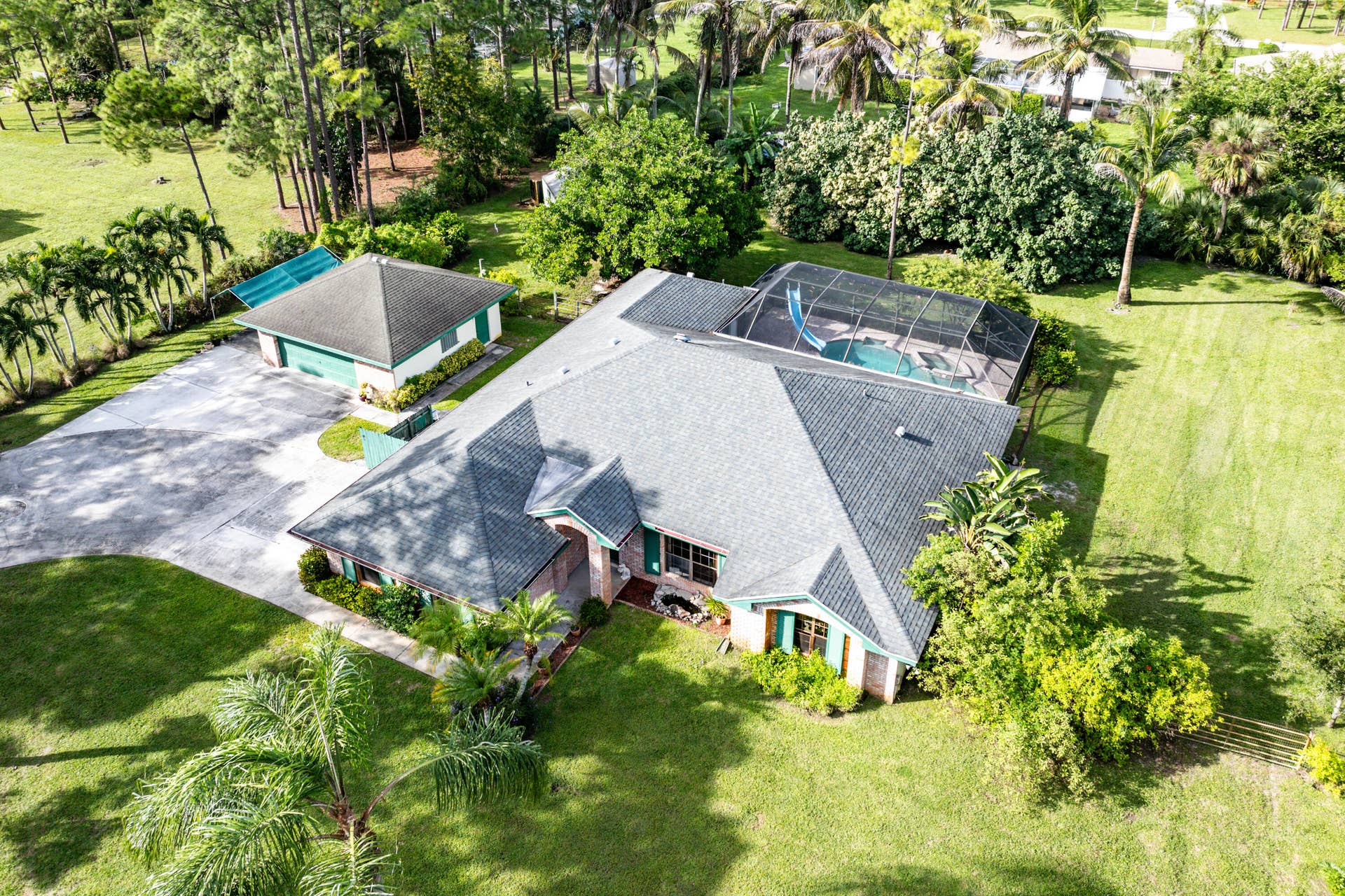 13677 Citrus Grove Boulevard, West Palm Beach, FL 33412 Aerial perspective featuring a shingled roof residence with a detached garage, a screened-in pool enclosure, and expansive landscaped grounds
