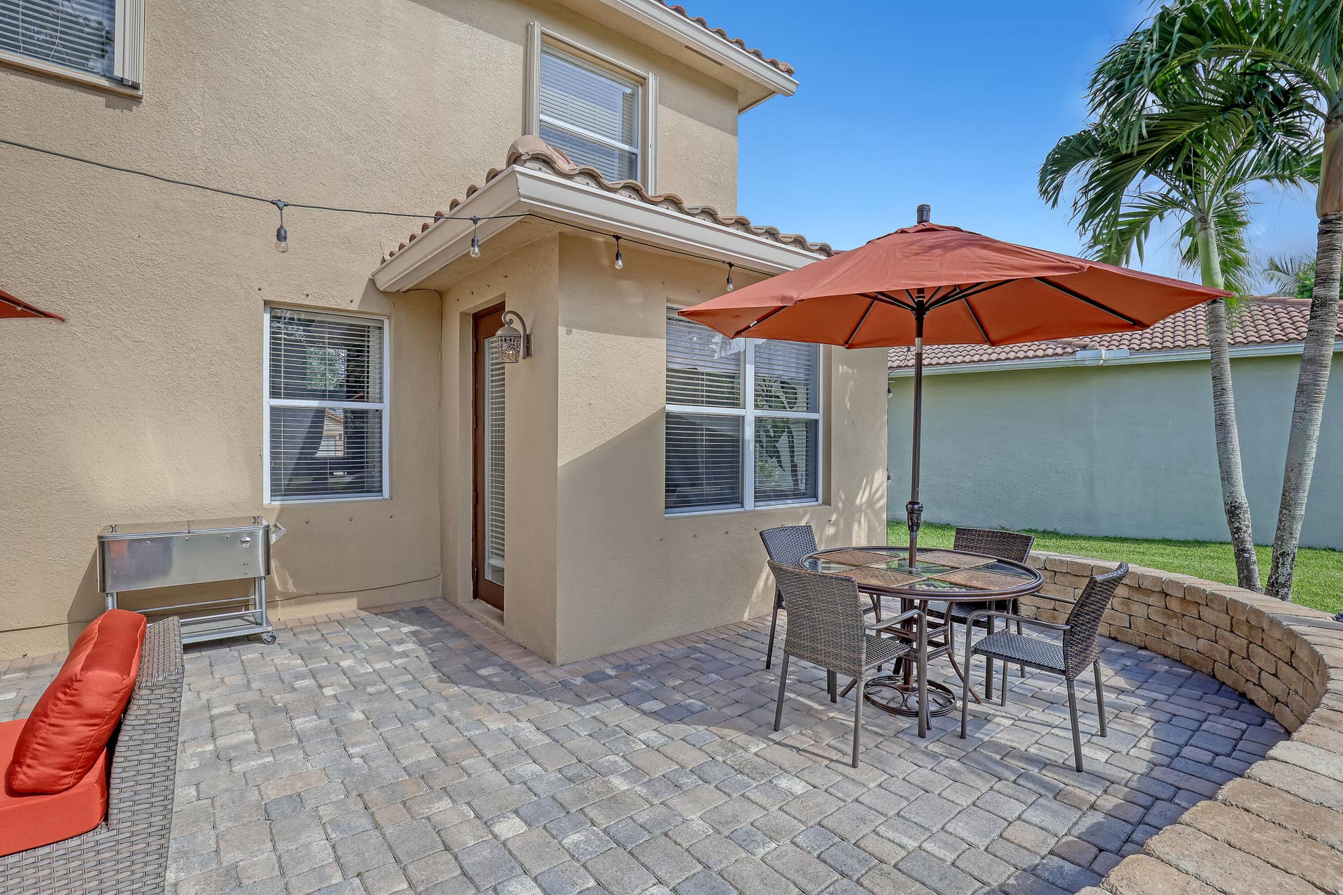 762 GAZETTA Way, West Palm Beach, FL 33413 Stucco exterior featuring a paver patio, integrated segmental retaining wall, and exterior string lighting