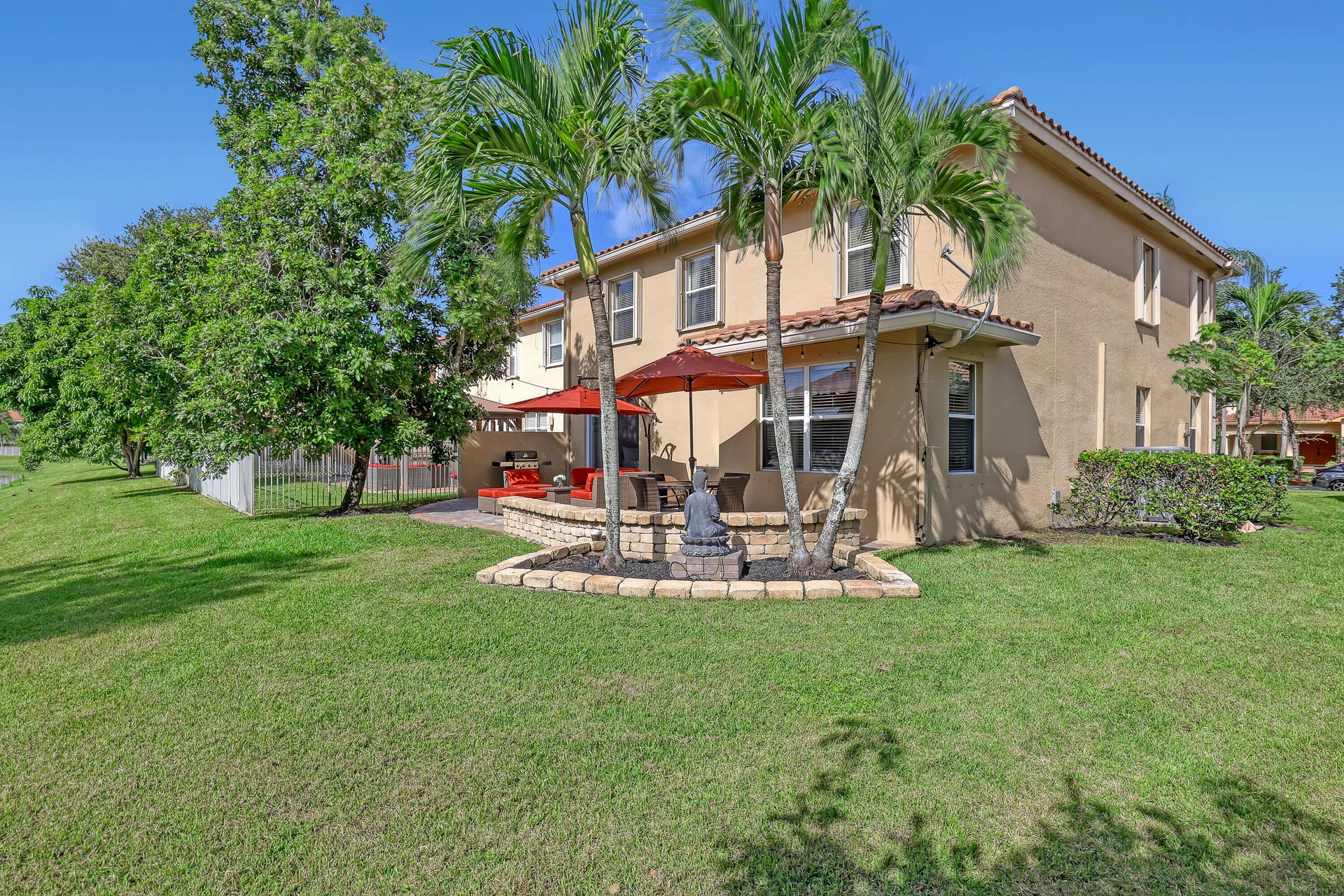762 GAZETTA Way, West Palm Beach, FL 33413 Rear exterior featuring a two-story stucco facade, tiled roof, paver patio, and decorative stone retaining wall with integrated palm trees