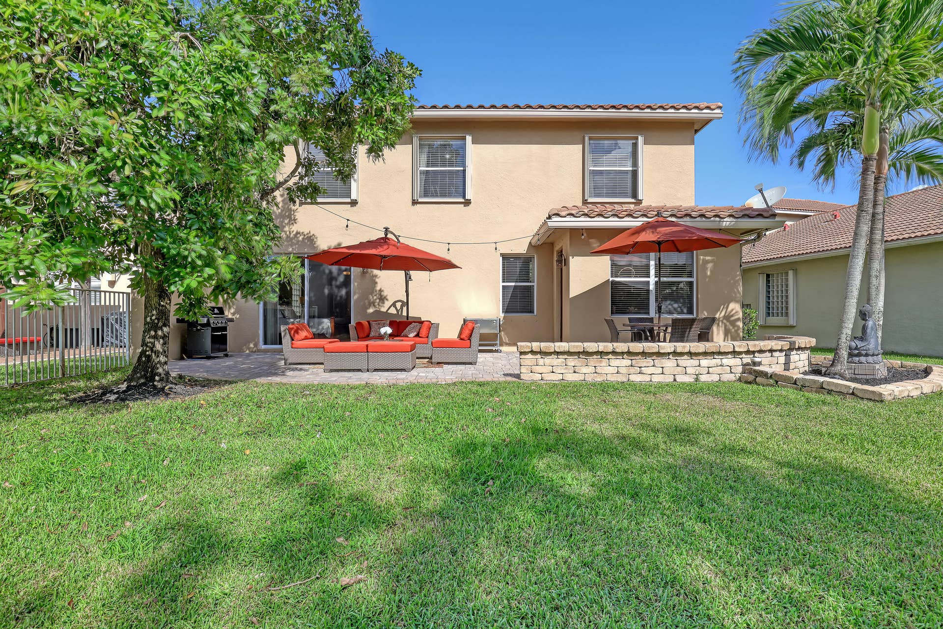 762 GAZETTA Way, West Palm Beach, FL 33413 Rear exterior featuring a stucco facade, tile roof, stone paver patio, and a tiered stone retaining wall