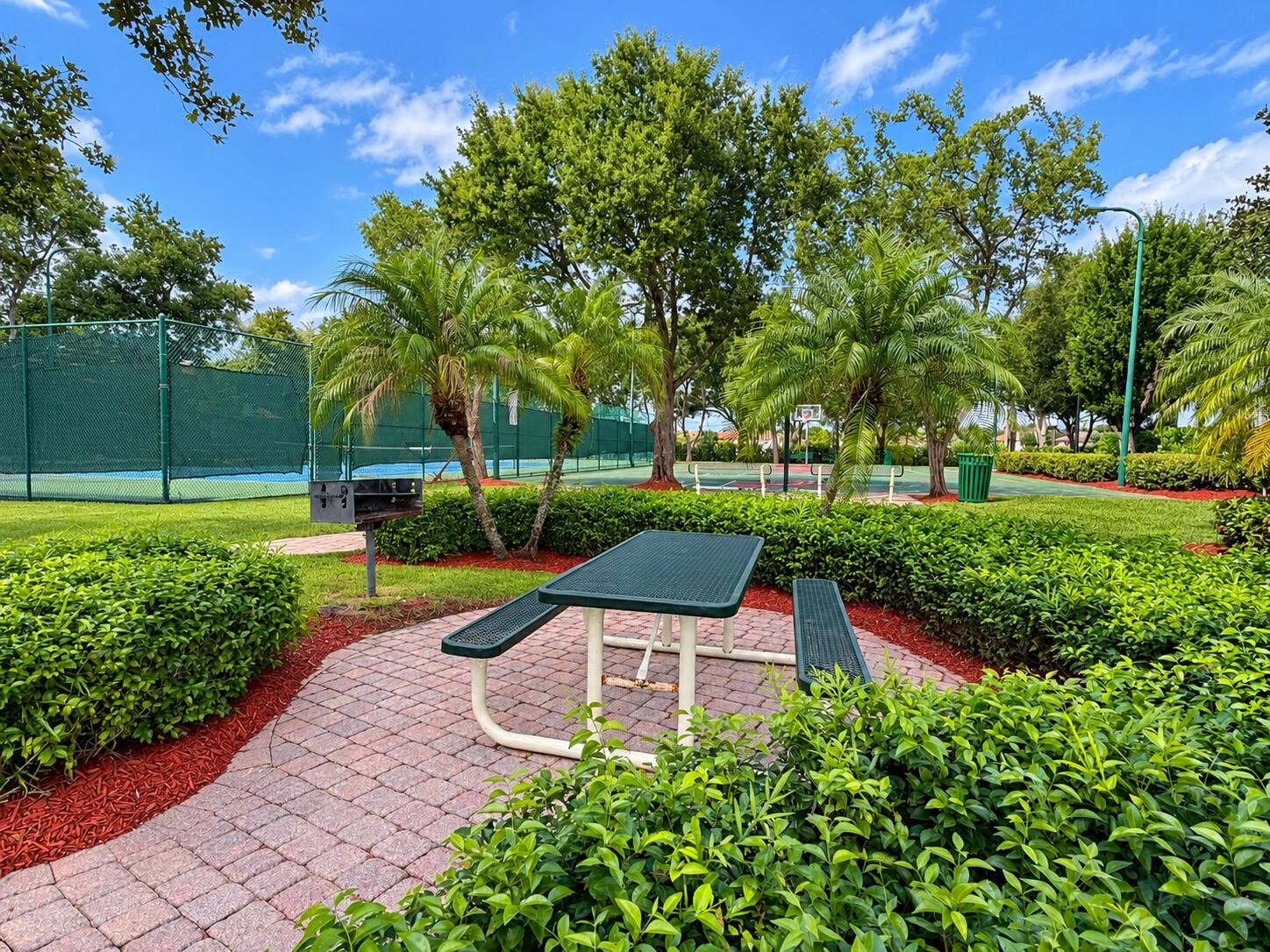 762 GAZETTA Way, West Palm Beach, FL 33413 Outdoor recreation area featuring a paved brick patio, built-in charcoal grill, tennis court, and manicured landscaping with mature trees and palms