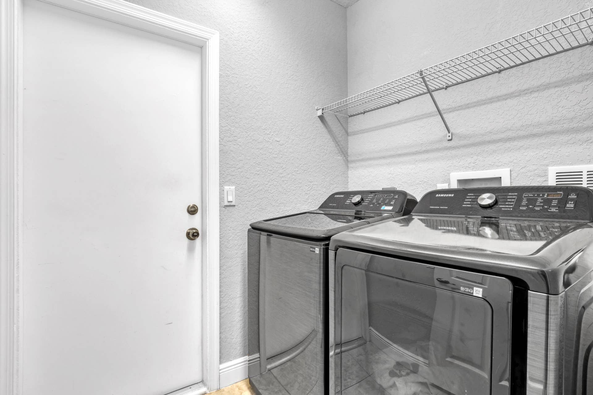 762 GAZETTA Way, West Palm Beach, FL 33413 Laundry space featuring metallic-finish top-load washer and dryer with glass lids, paired with an integrated wall-mounted wire shelving unit and a solid-core entry door to garage