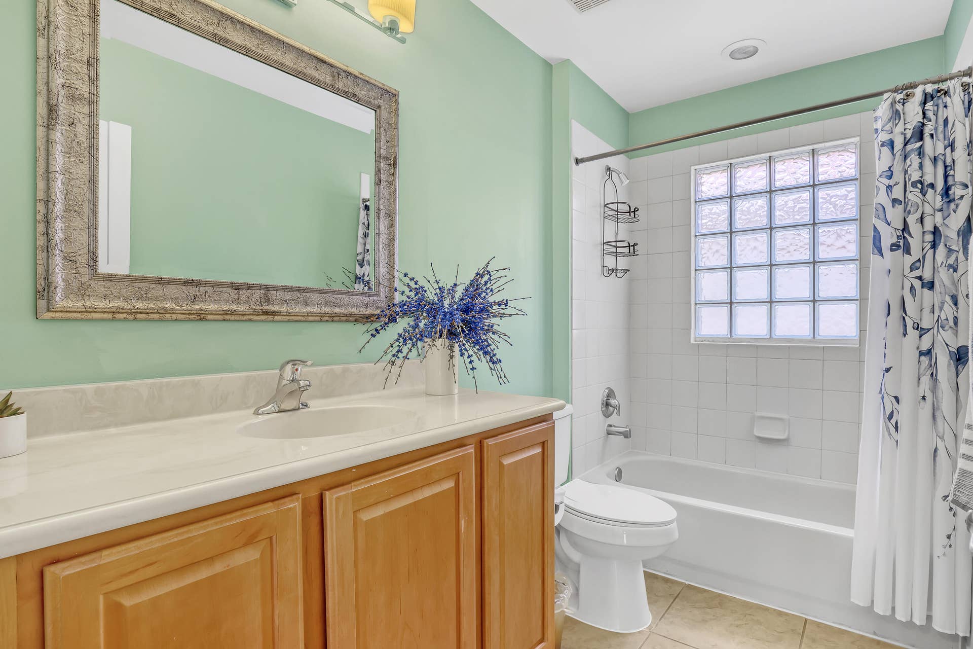 762 GAZETTA Way, West Palm Beach, FL 33413 Bathroom featuring a vanity with integrated sink and countertop, framed wall mirror, glass block window, and a tiled bathtub surround