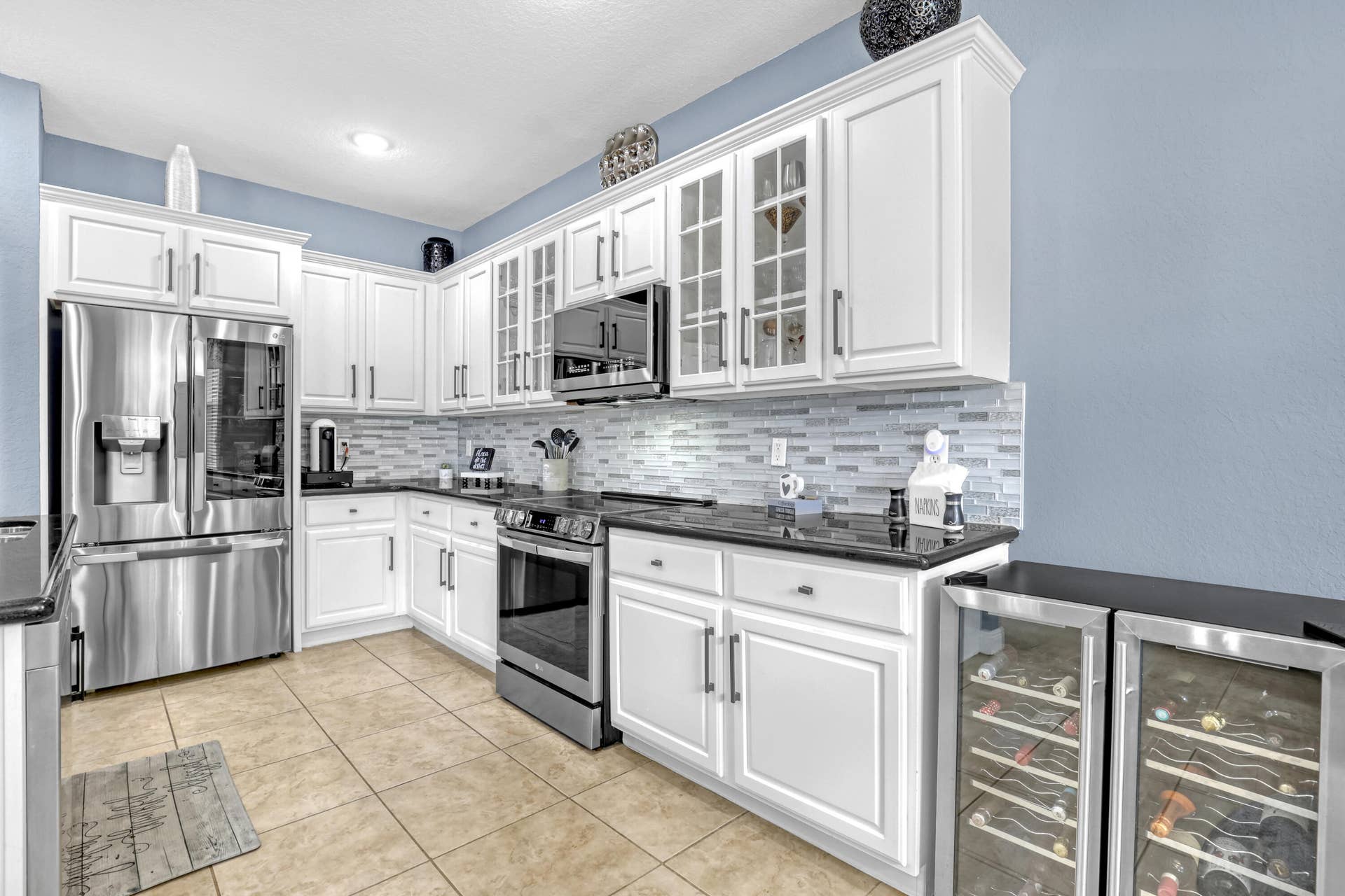 762 GAZETTA Way, West Palm Beach, FL 33413 Kitchen featuring white shaker-style cabinetry with glass-front accents, polished granite countertops, stainless steel appliances, a linear-patterned tile backsplash