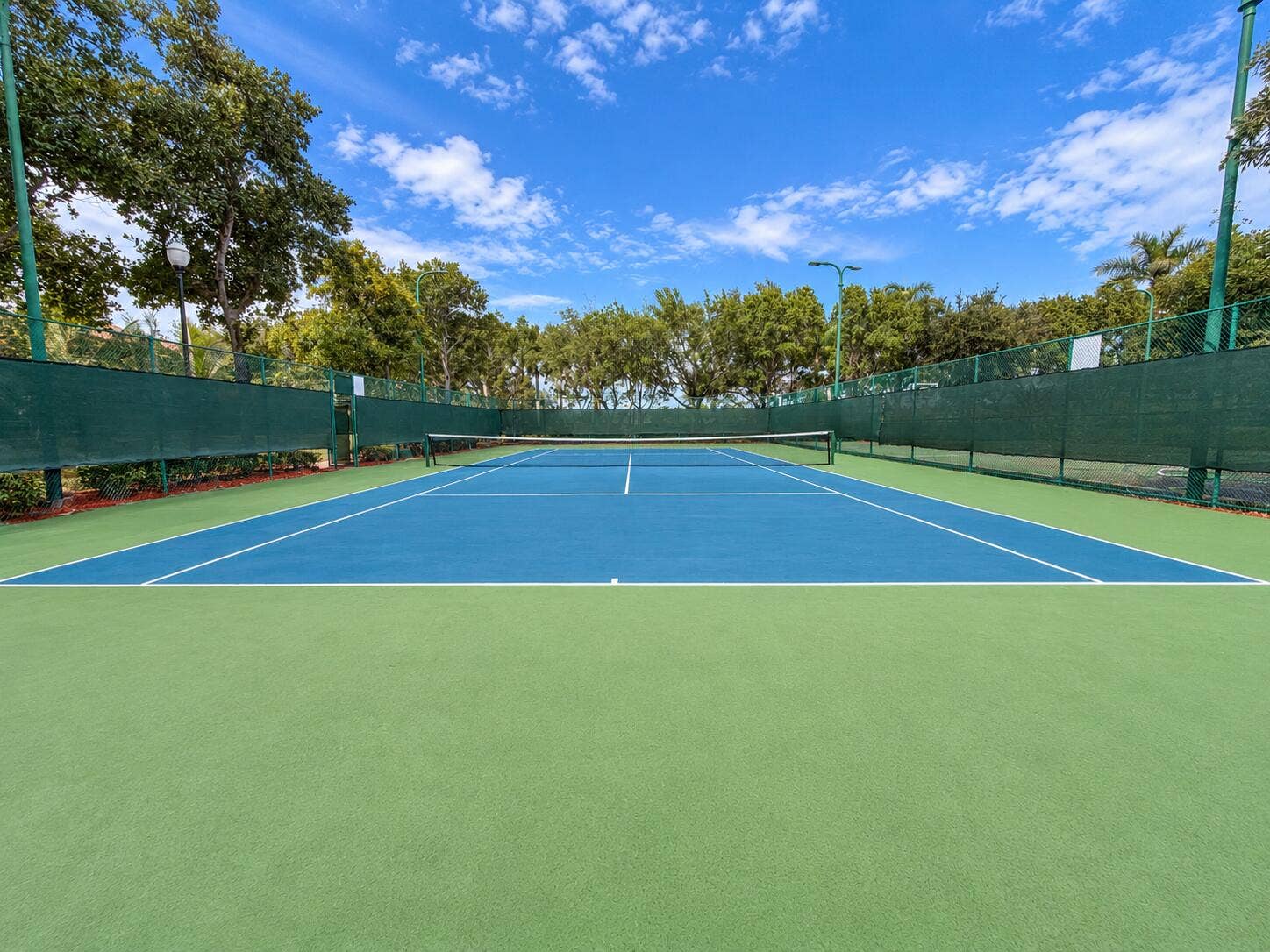 762 GAZETTA Way, West Palm Beach, FL 33413 Private tennis court featuring a hard-surface finish, perimeter fencing, overhead lighting, and surrounding mature landscaping