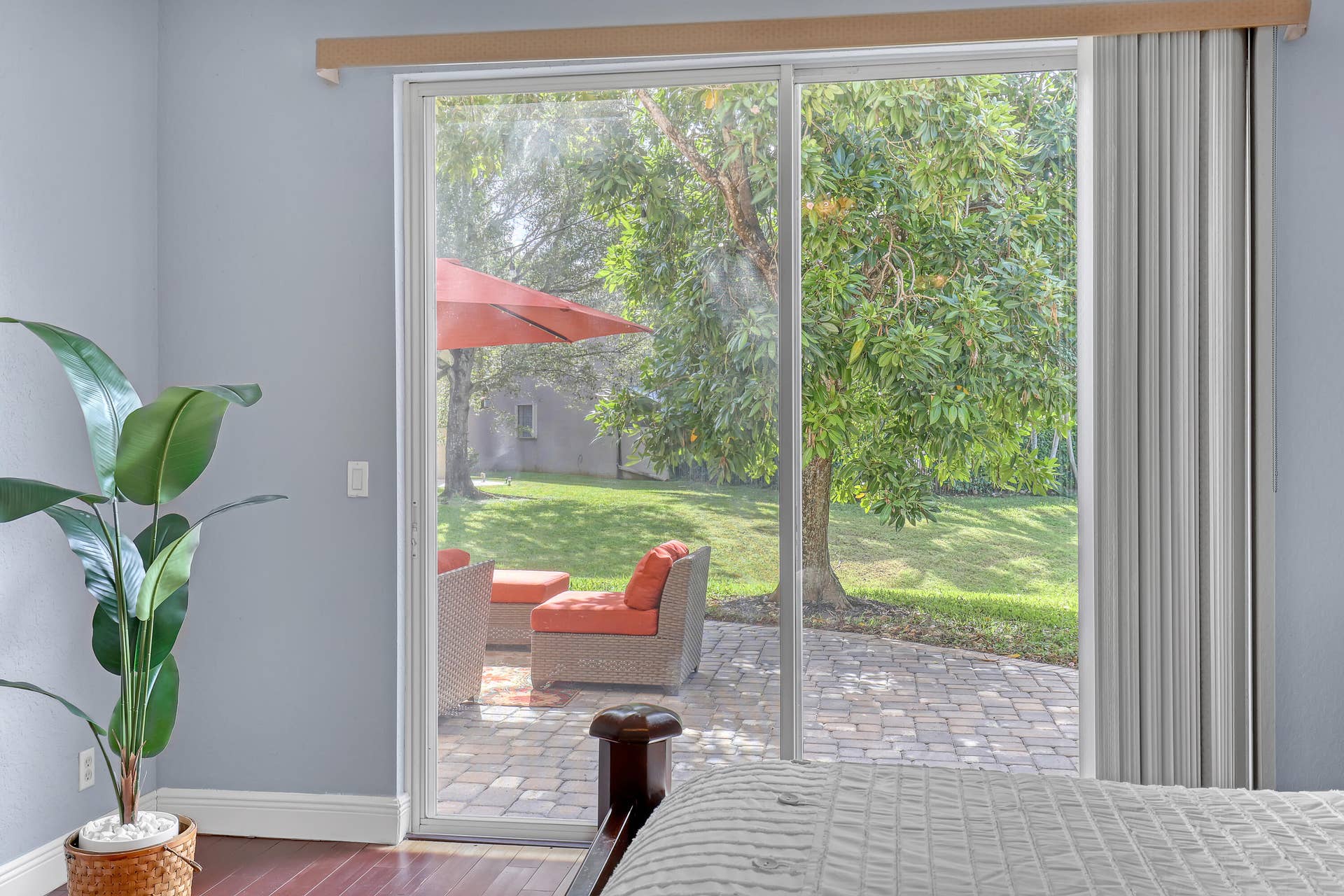 762 GAZETTA Way, West Palm Beach, FL 33413 Sliding glass door with vertical blinds opening to a paved stone patio, mature trees, and a grass lawn