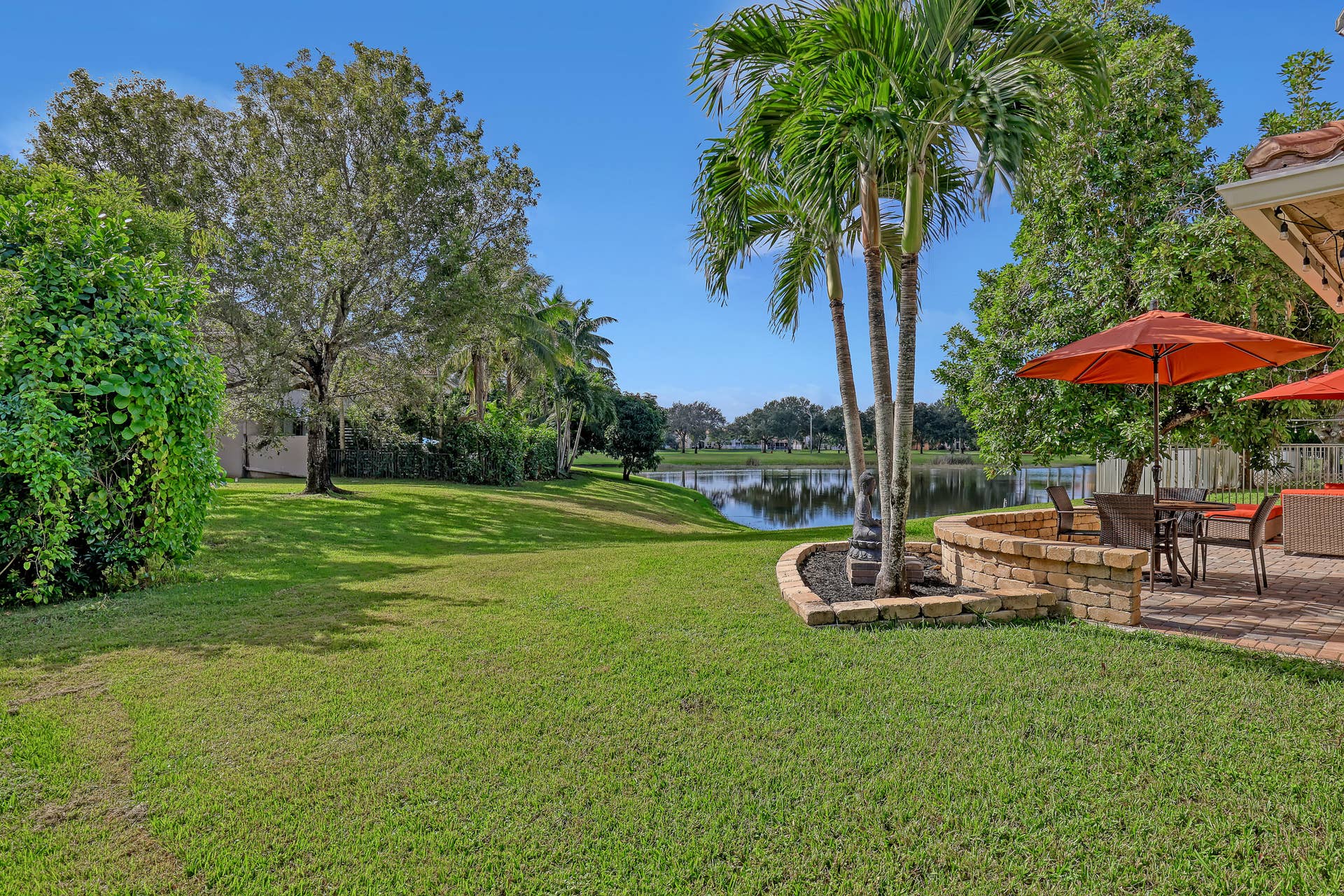 762 GAZETTA Way, West Palm Beach, FL 33413 Expansive lawn, water frontage, mature palms, and brick-paver patio with a stone-finish retaining wall