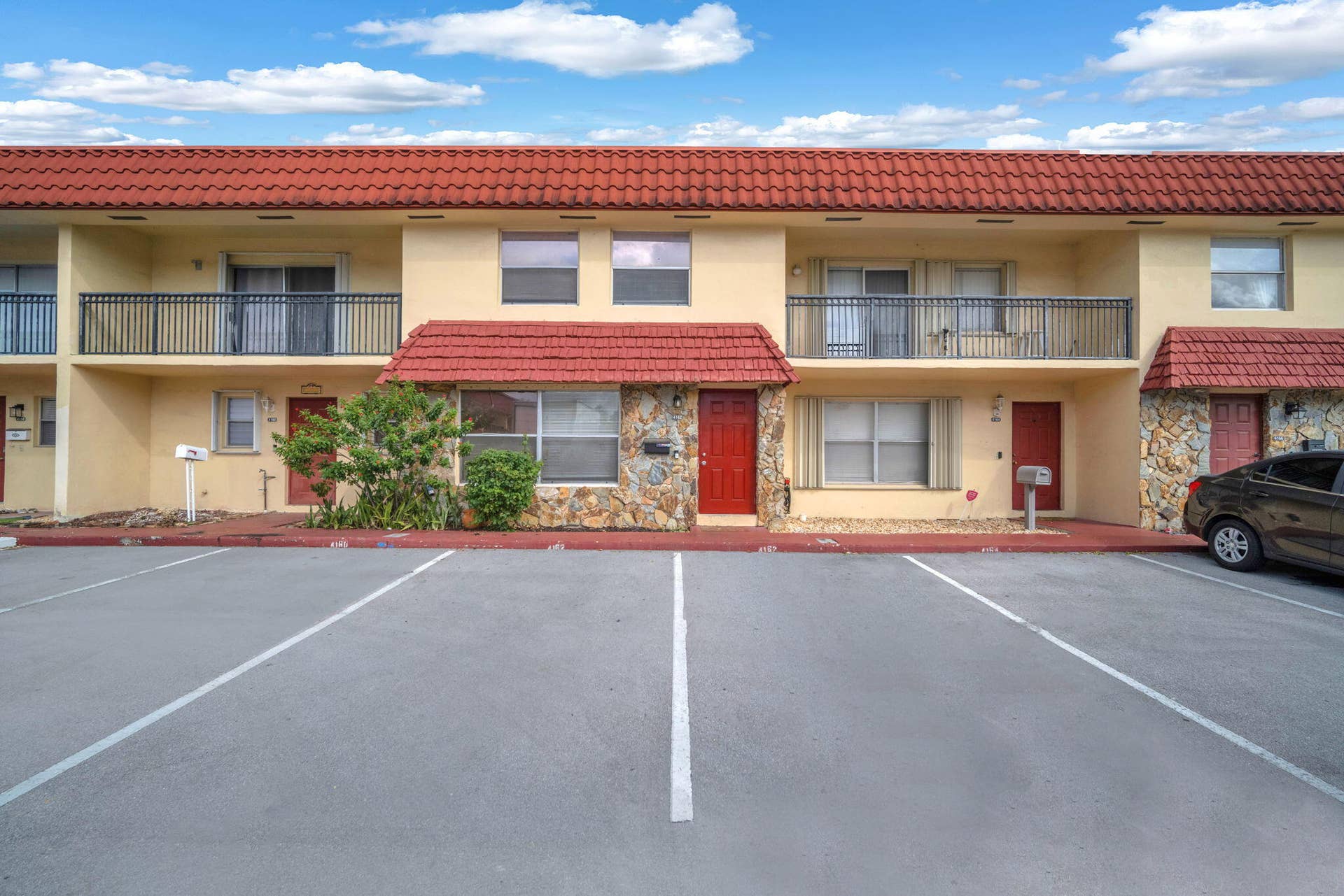 4162 SW 65th Avenue, #84, Davie, FL 33314 Exterior facade featuring a terra cotta tile roof, stone masonry accents, second-story balconies with iron railings, and dedicated off-street parking