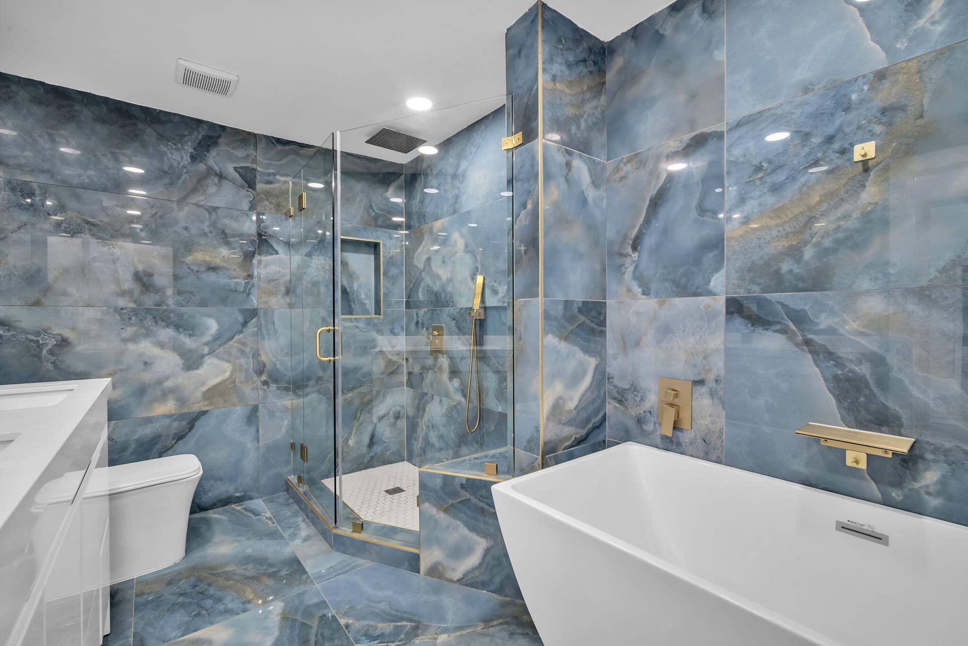 4162 SW 65th Avenue, #84, Davie, FL 33314 Large-format blue stone wall and floor tiling, freestanding white soaking tub, walk-in glass-enclosed shower with a recessed niche, and gold-finish plumbing fixtures
