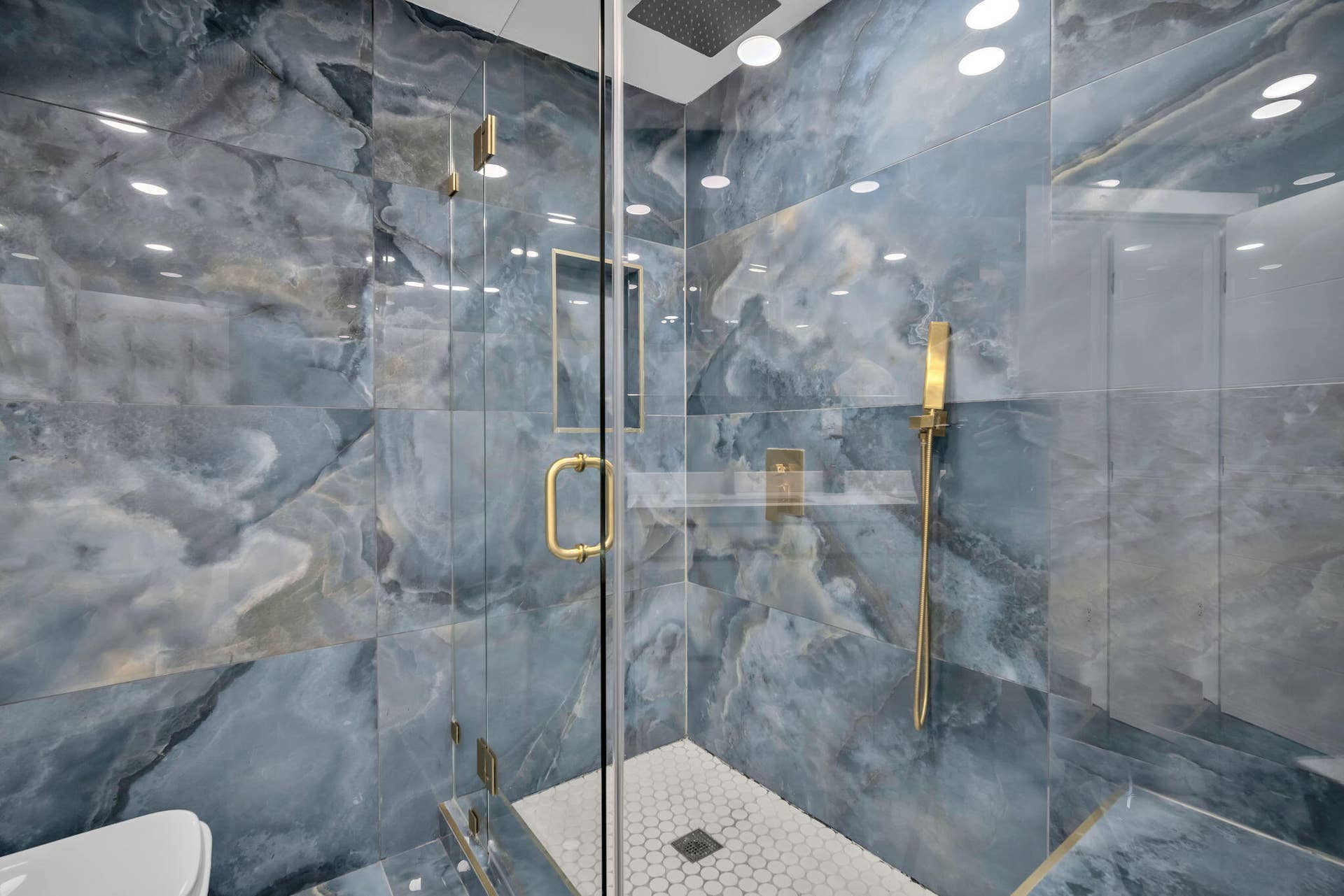 4162 SW 65th Avenue, #84, Davie, FL 33314 Walk-in shower featuring large-format blue stone-finish wall tile, gold-toned hardware, rainfall showerhead, integrated wall niche, and hexagonal floor tile