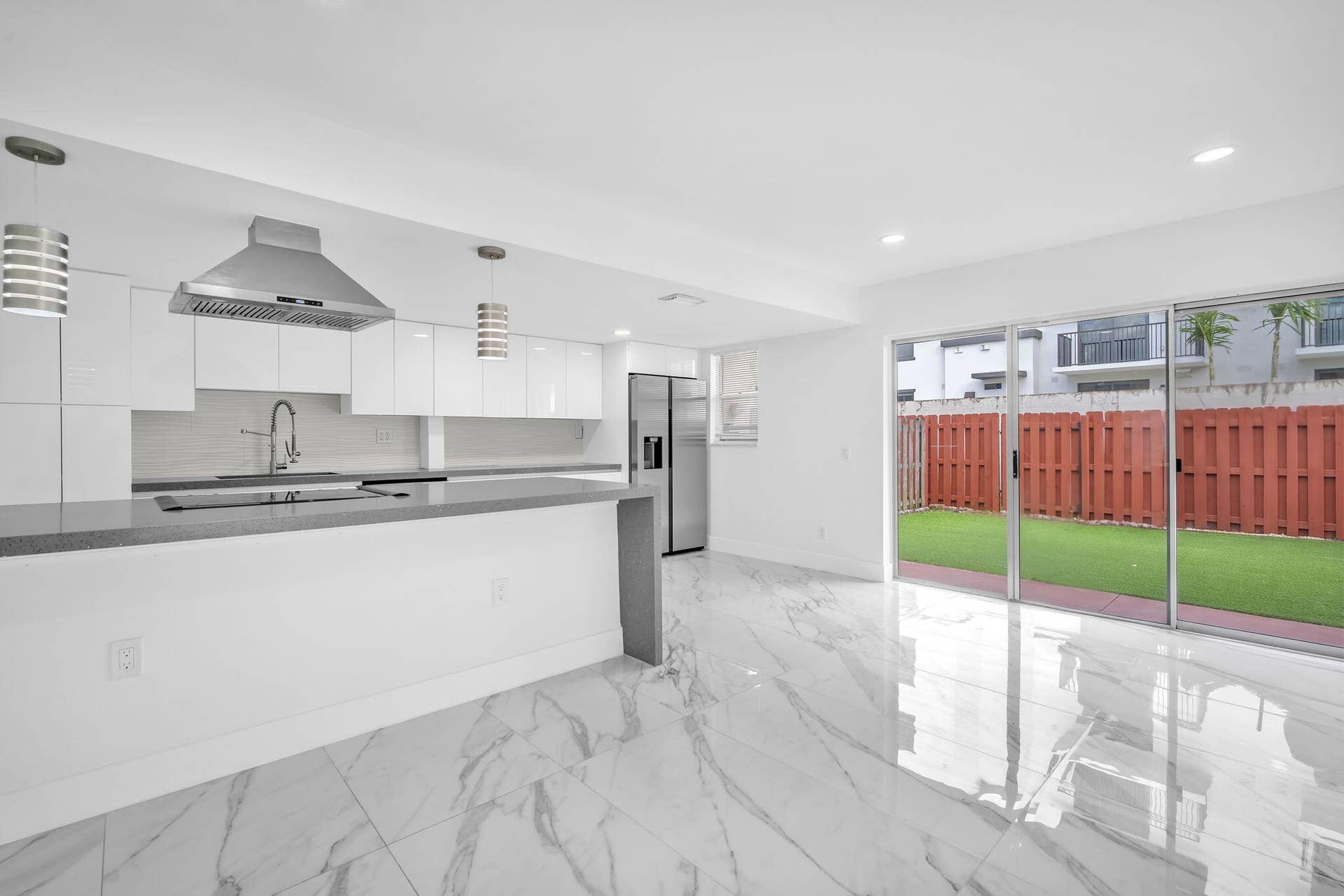 4162 SW 65th Avenue, #84, Davie, FL 33314 Kitchen featuring white cabinetry, stainless steel range hood, stone-surface peninsula, and large-format tile flooring with recessed lighting, paired with sliding glass doors leading to a fenced backyard