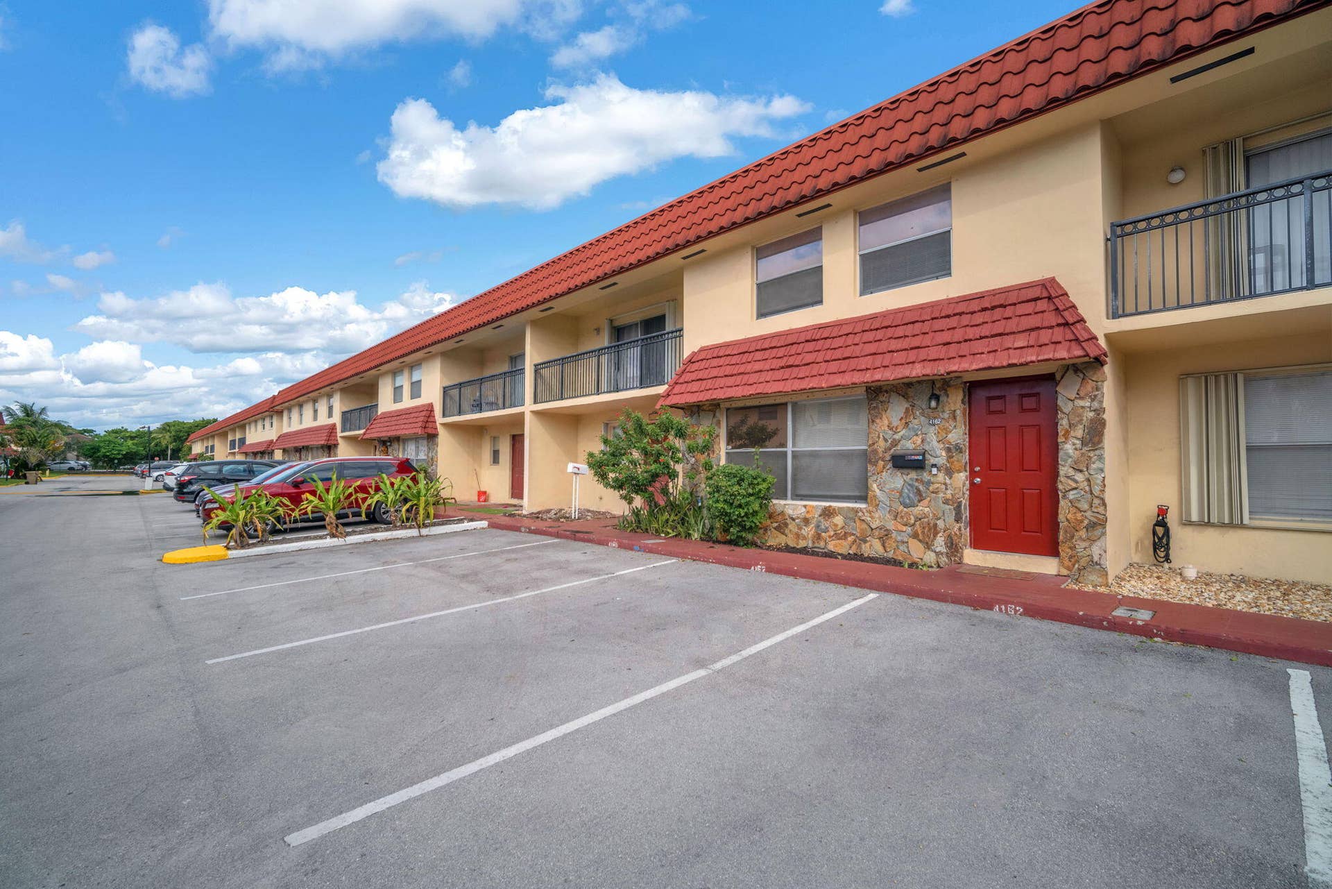 4162 SW 65th Avenue, #84, Davie, FL 33314 Two-story building exterior featuring a red tile roof, stone veneer accents, second-story metal railed balconies, and assigned surface parking