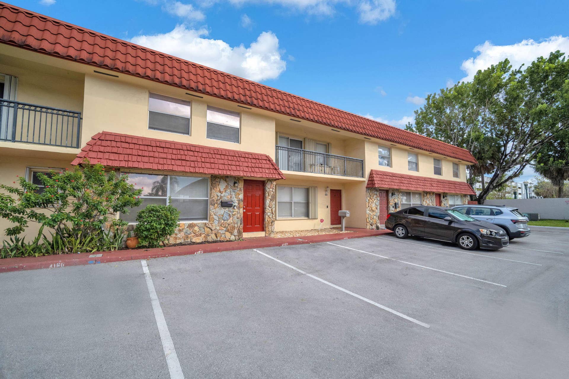 4162 SW 65th Avenue, #84, Davie, FL 33314 Two-story exterior featuring a Spanish tile roof, stone masonry facade, red entry doors, and metal balcony railings