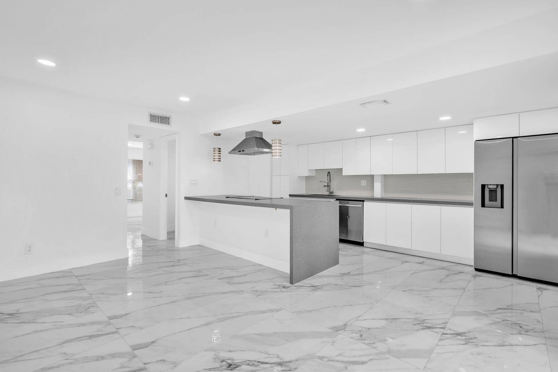 4162 SW 65th Avenue, #84, Davie, FL 33314 Modern kitchen featuring white flat-panel cabinetry, a waterfall-edge island with an integrated cooktop, polished stone-finish floor tiling, recessed lighting, and stainless steel appliances