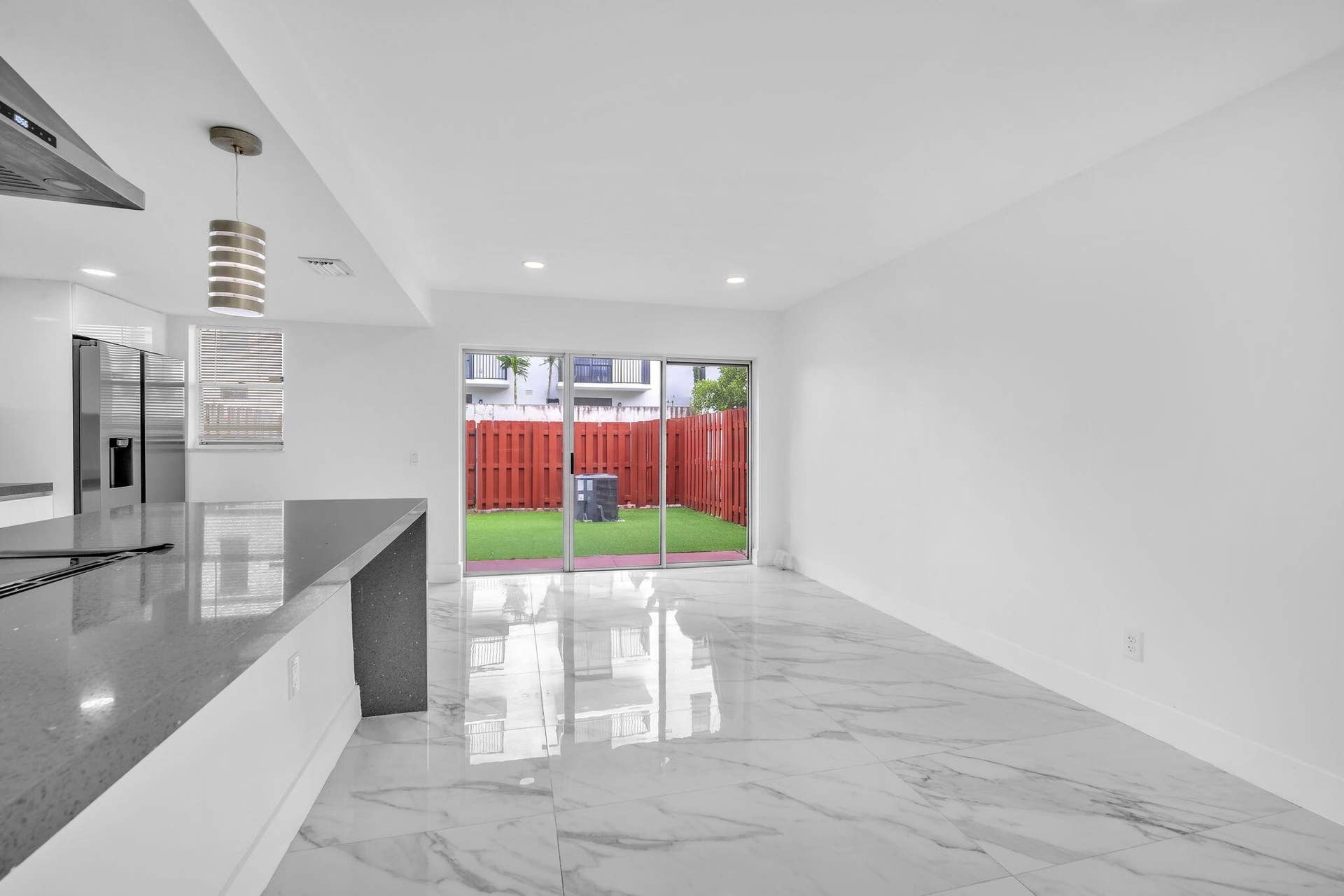 4162 SW 65th Avenue, #84, Davie, FL 33314 Open-concept interior featuring large-format tile flooring, quartz waterfall kitchen island, sliding glass doors, recessed lighting, and a fenced exterior patio area